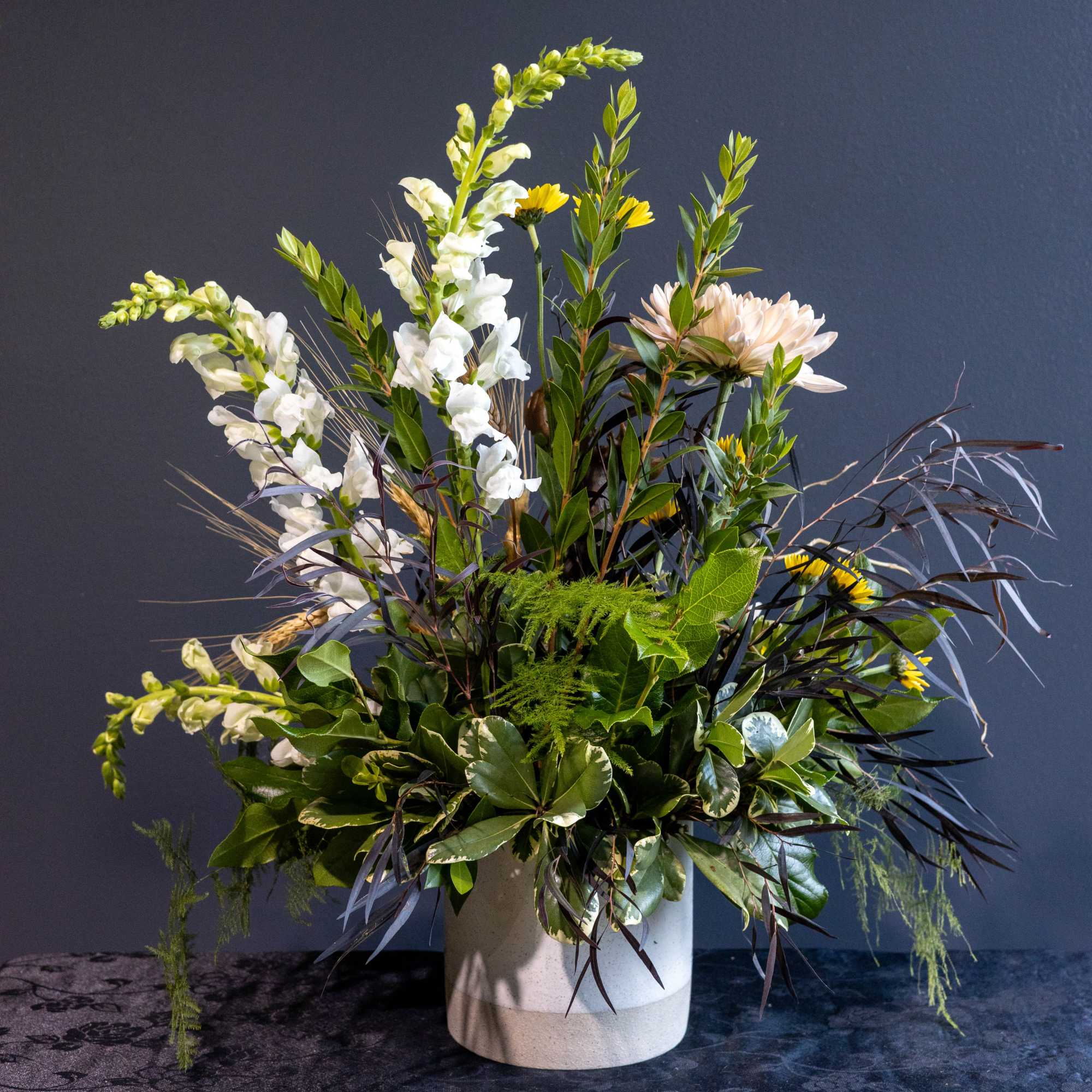 Tall mixed floral arrangement in a white vase with white and yellow blooms