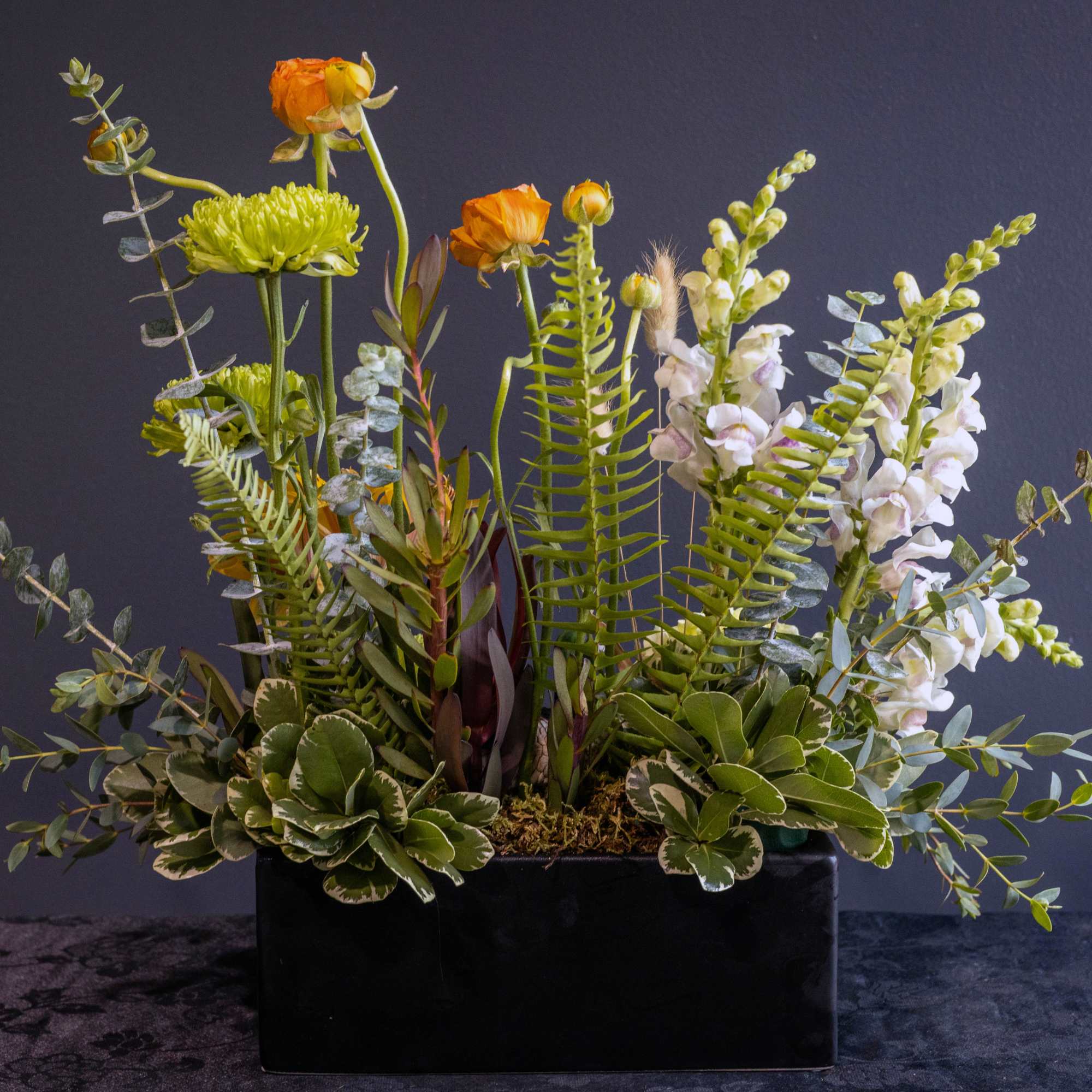 Mixed floral arrangement in a black rectangular container with orange and white blooms