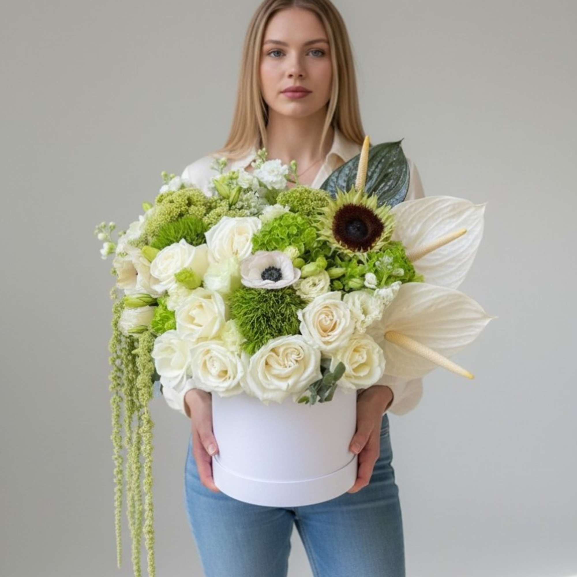 White and green floral arrangement in a round box held by a woman