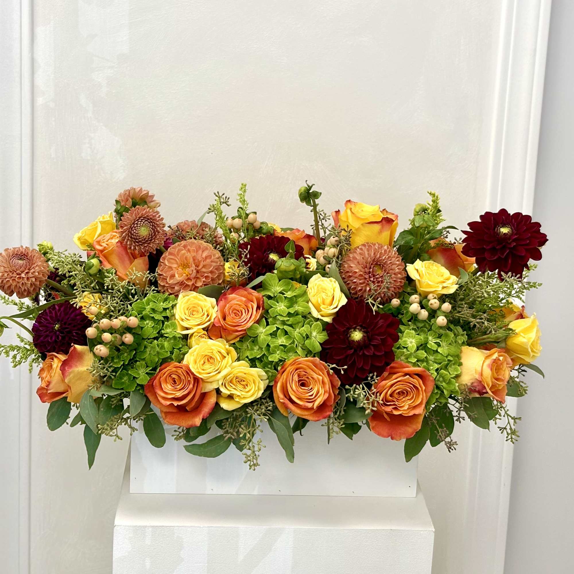 Mixed bouquet of orange, yellow, and burgundy flowers in a white container