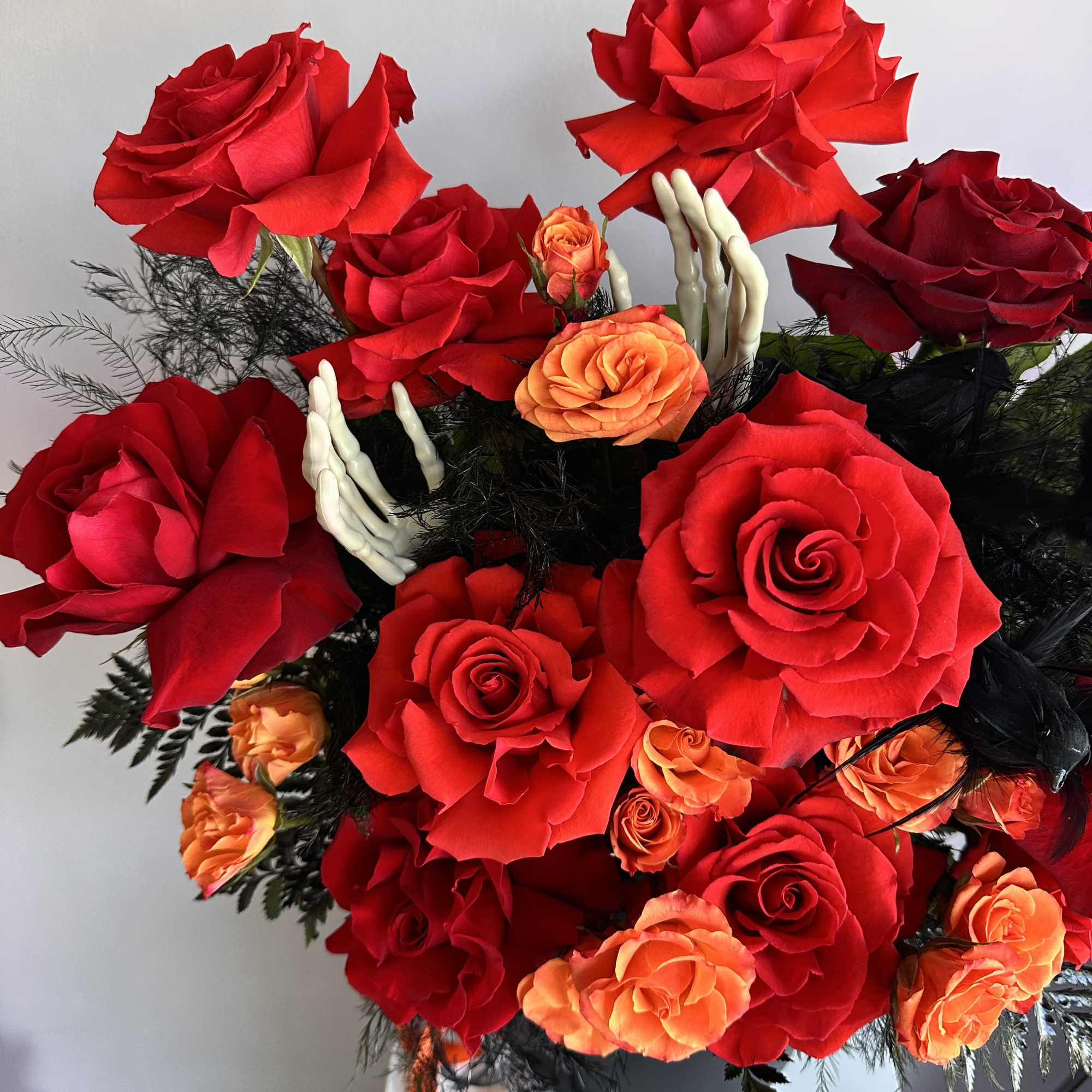 Red and orange rose arrangement with black accents and white skeleton hands