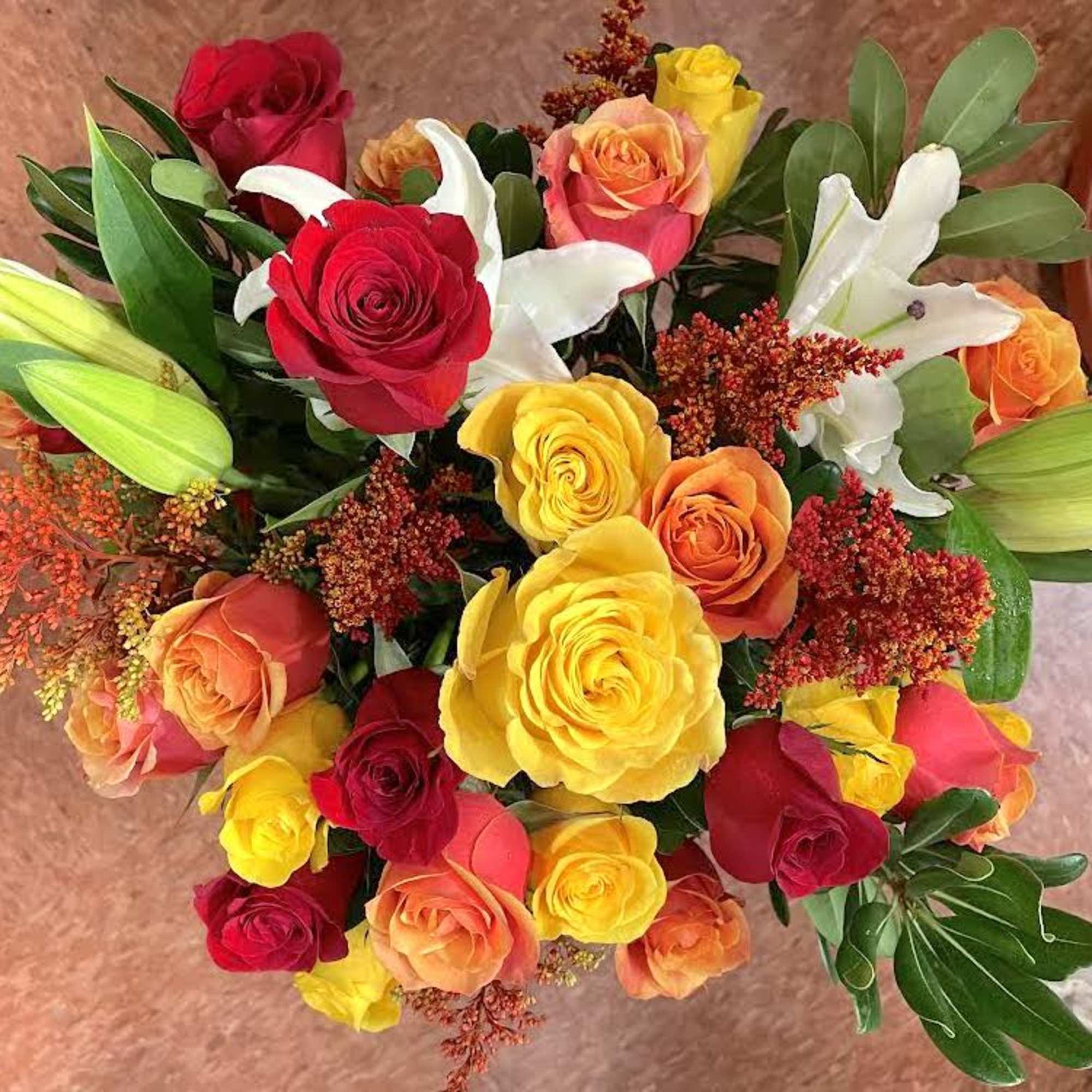 Top view of bright bouquet of red, yellow, and orange roses with white lilies