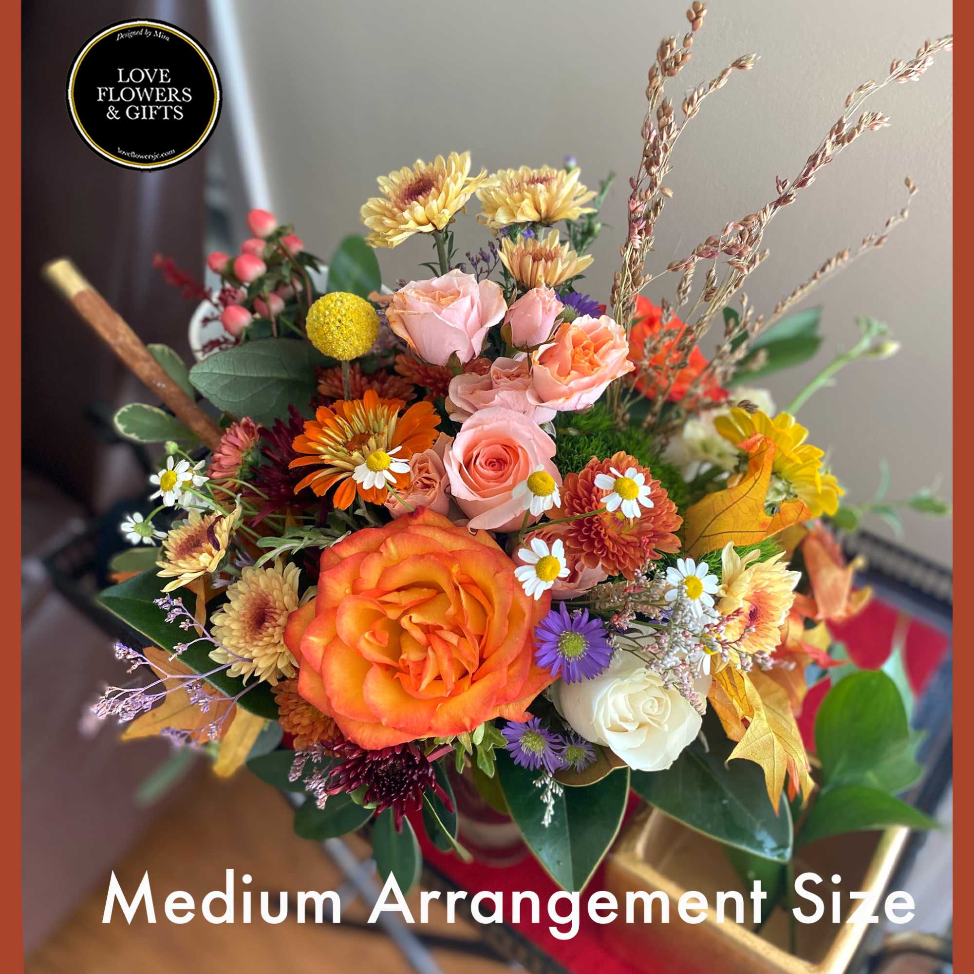 Autumn-toned arrangement of orange and peach roses with mixed daisies and mums in a medium glass vase