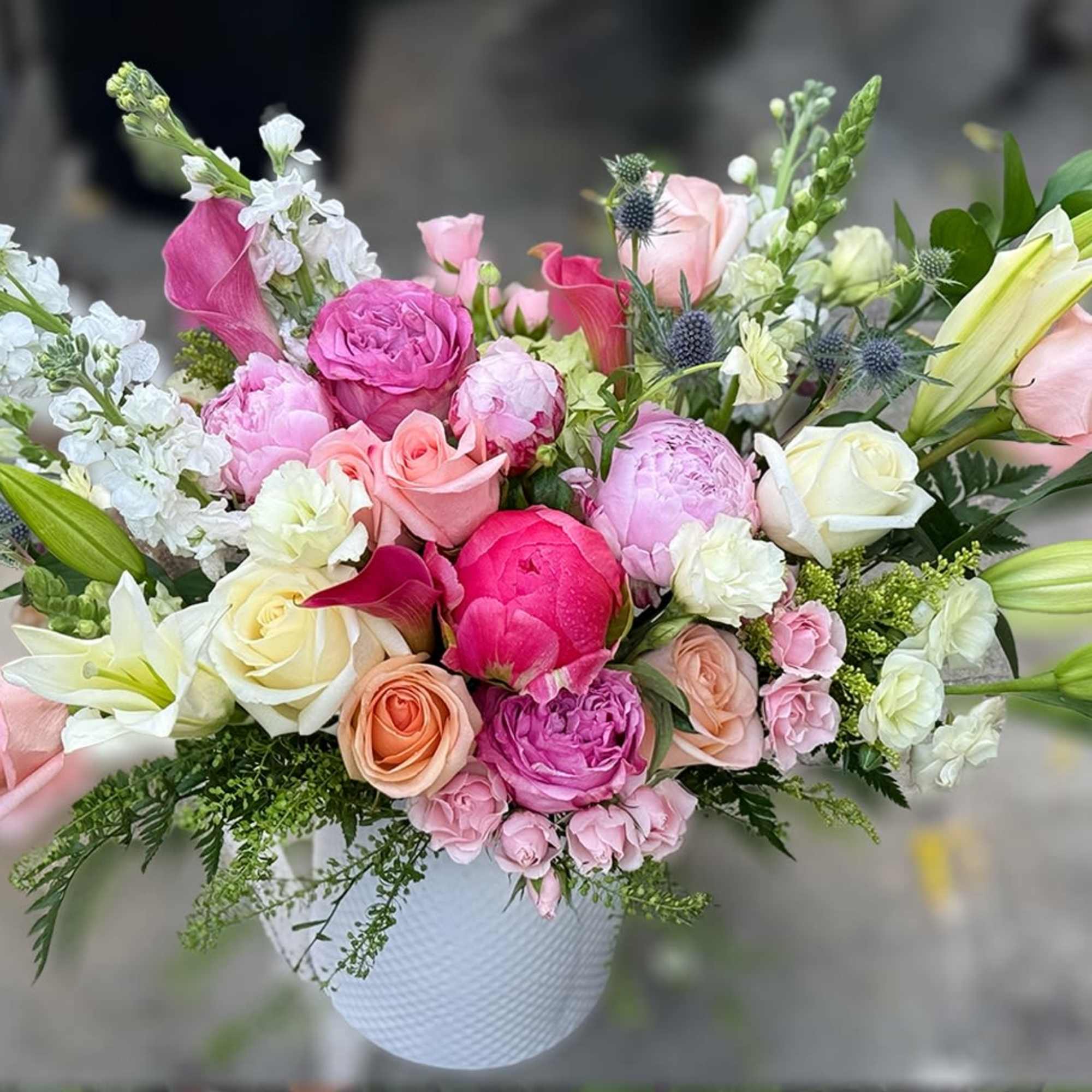 Mixed arrangement of pink peonies, roses, and lilies in a white ceramic vase