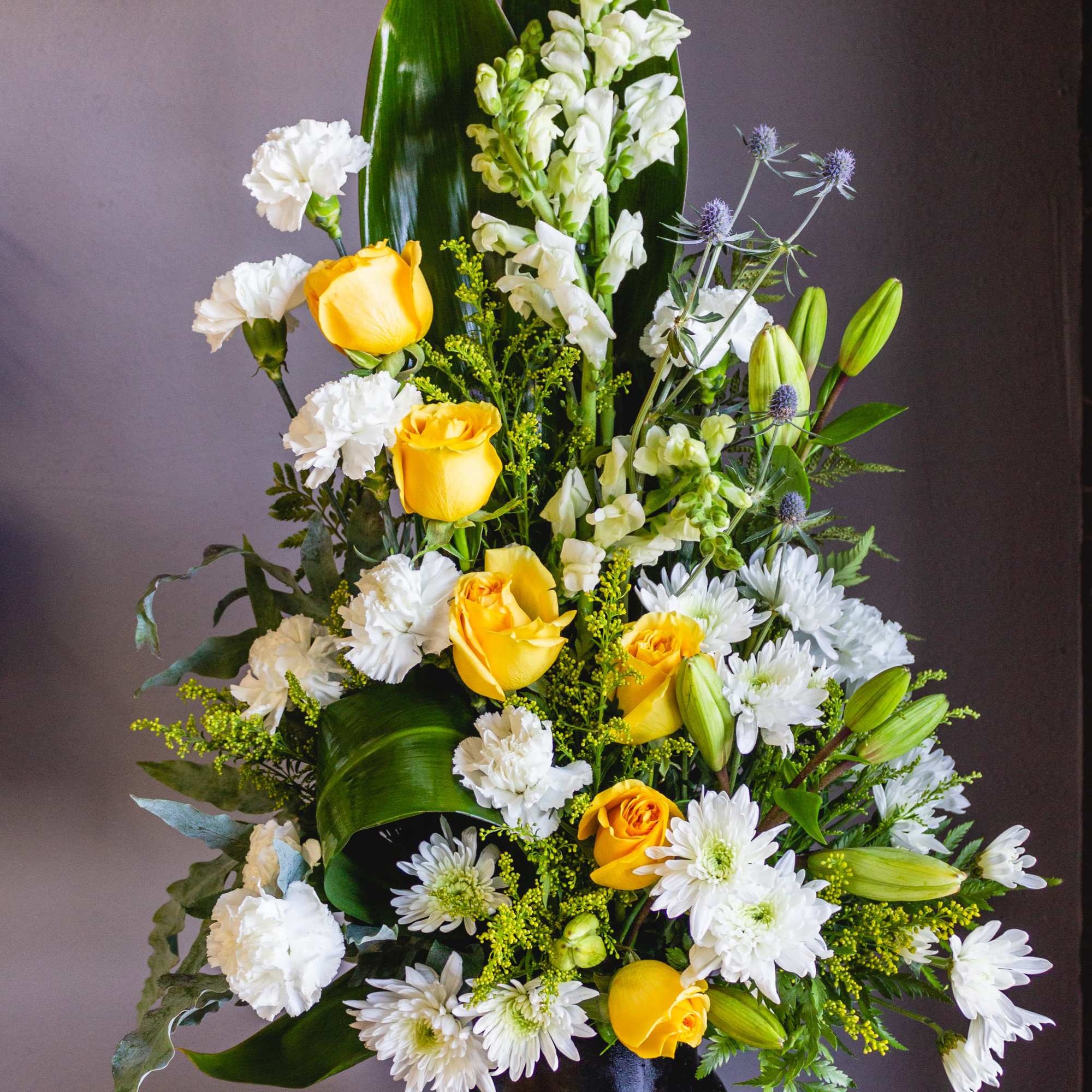 Tall floral arrangement with yellow roses, white blooms, and a black vase