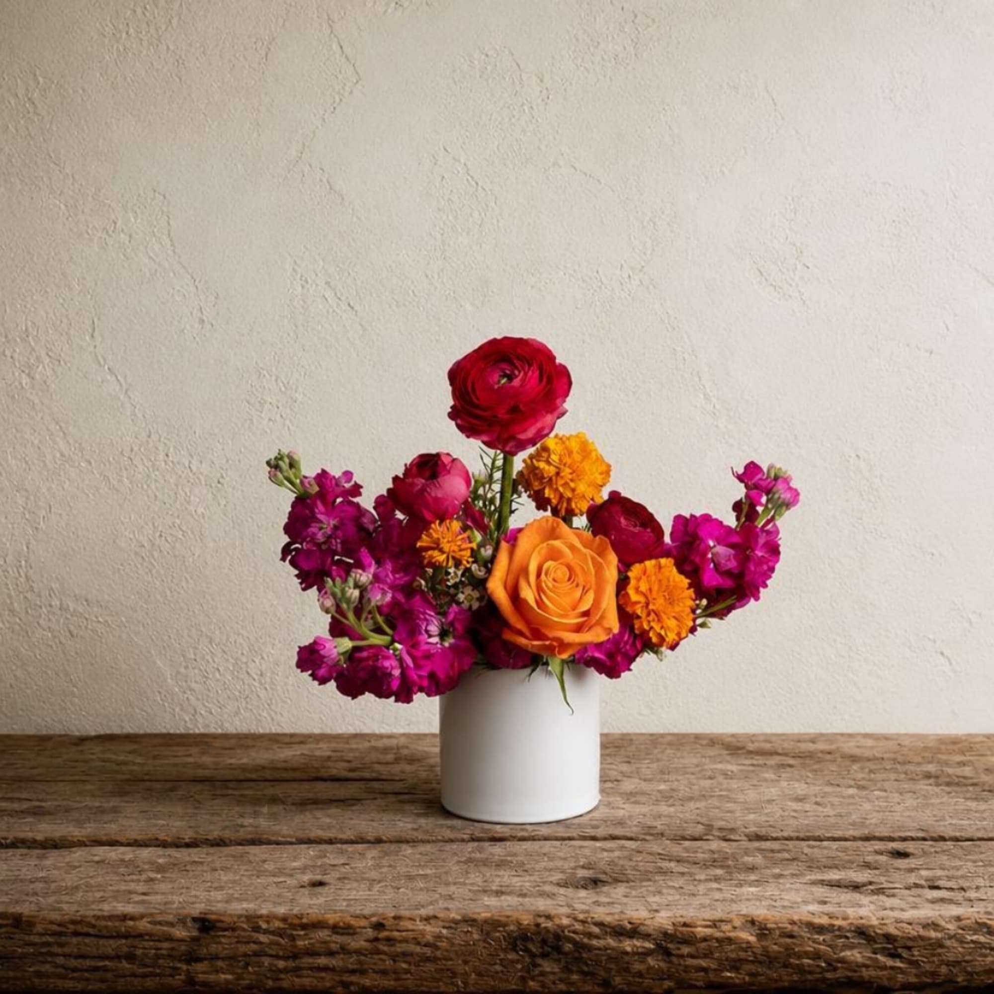 Colorful mixed flower arrangement in a white vase on a wooden table