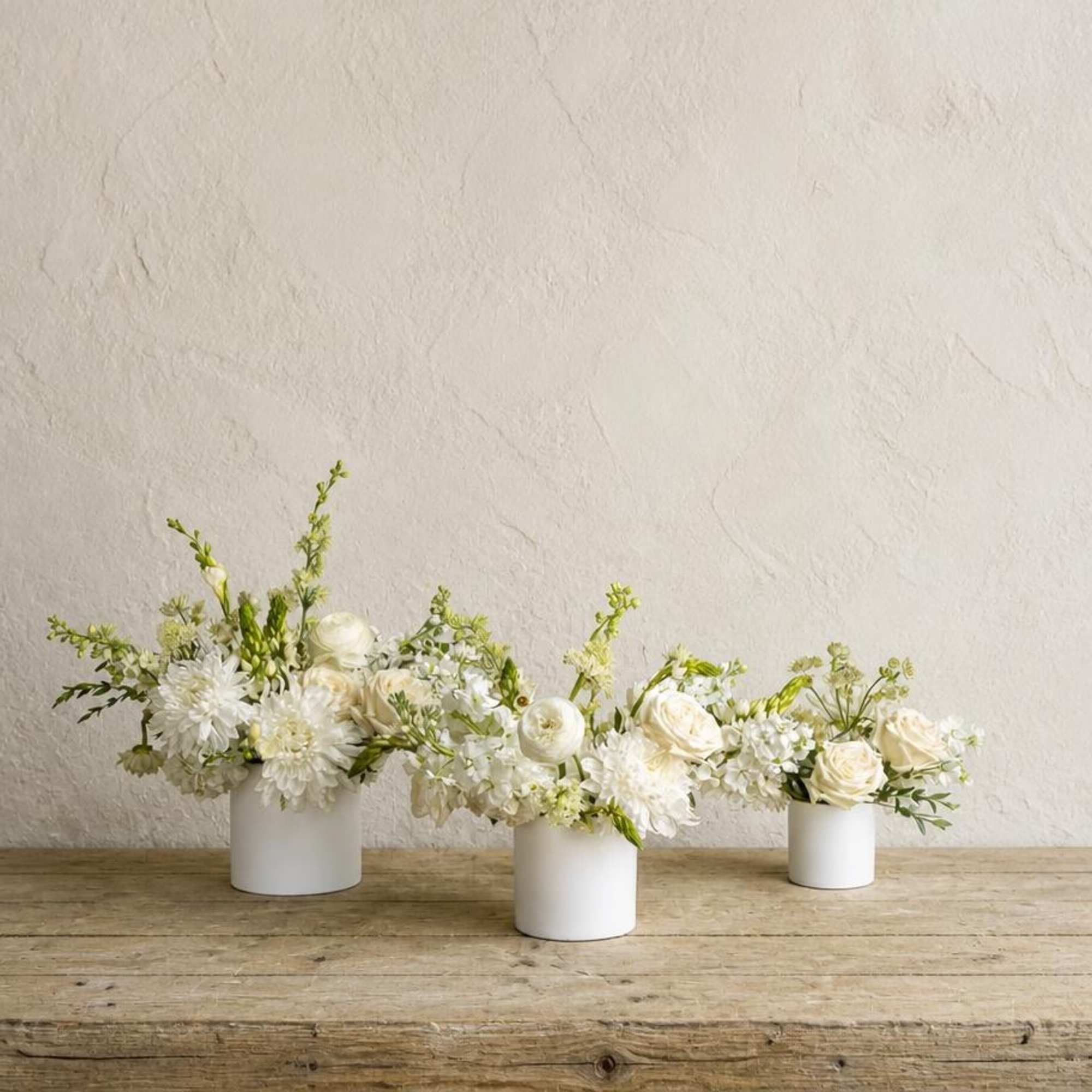 Three low white floral arrangements in small white containers