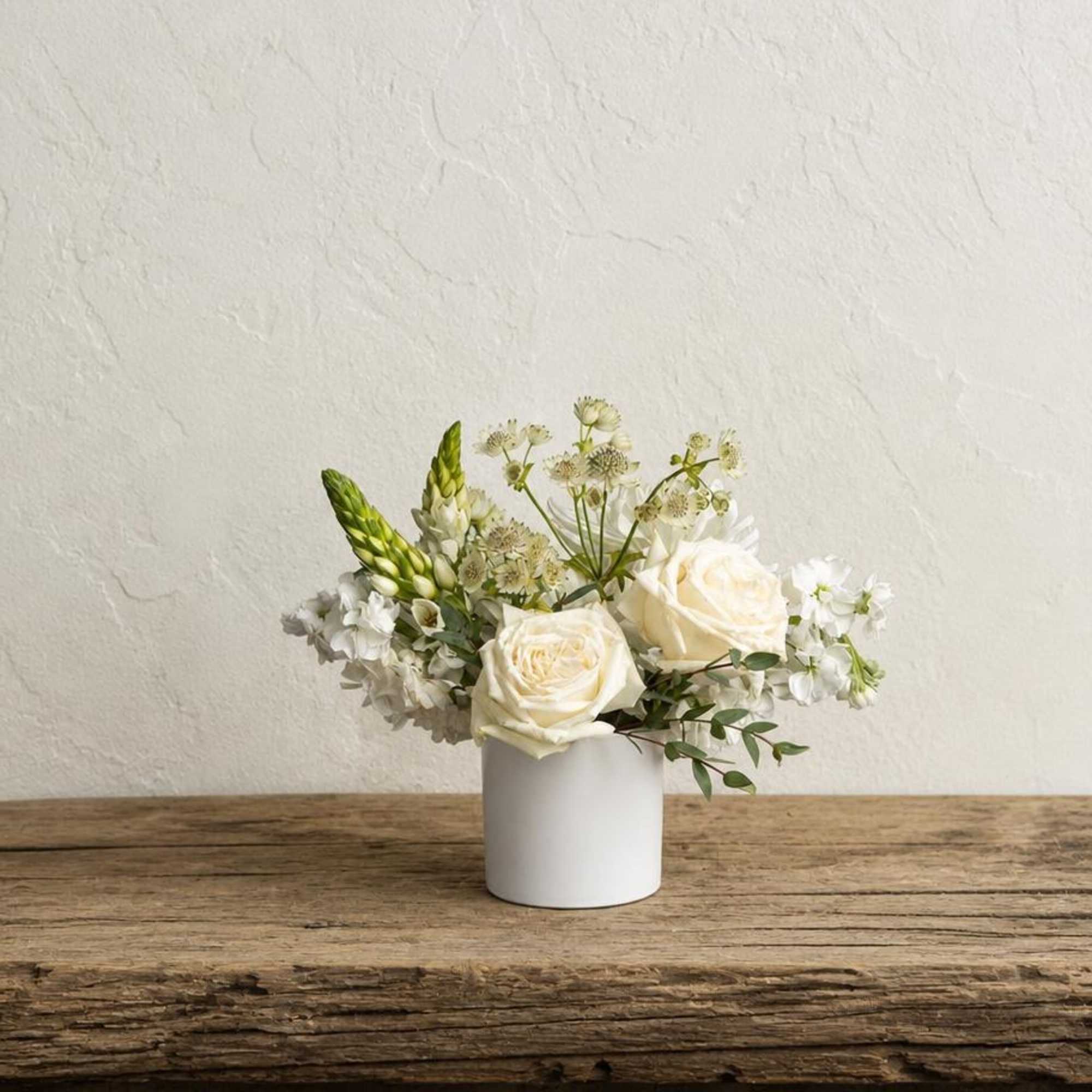 White roses and small white flowers arranged in a white vase