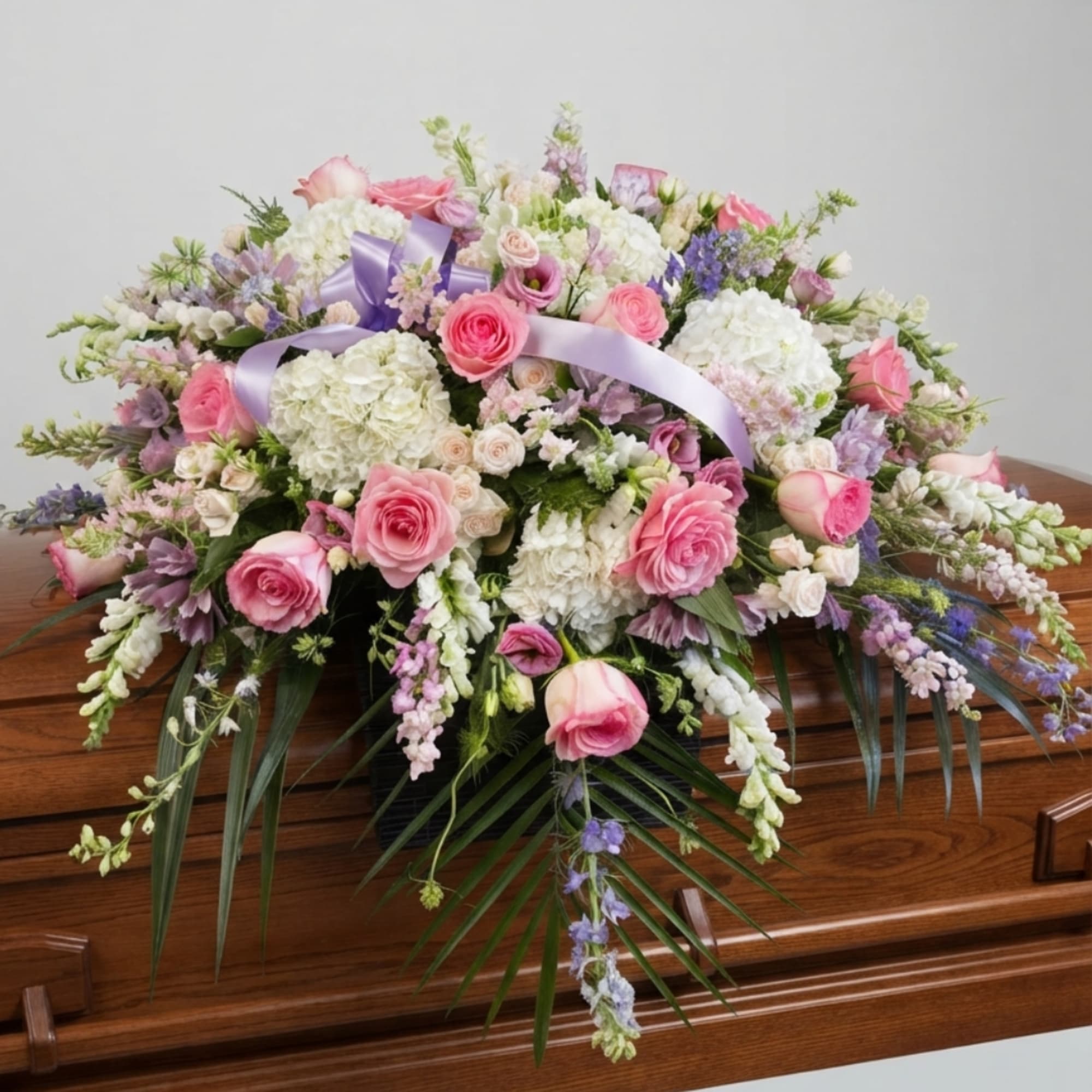 Large pink and white floral spray with ribbon on a wooden casket