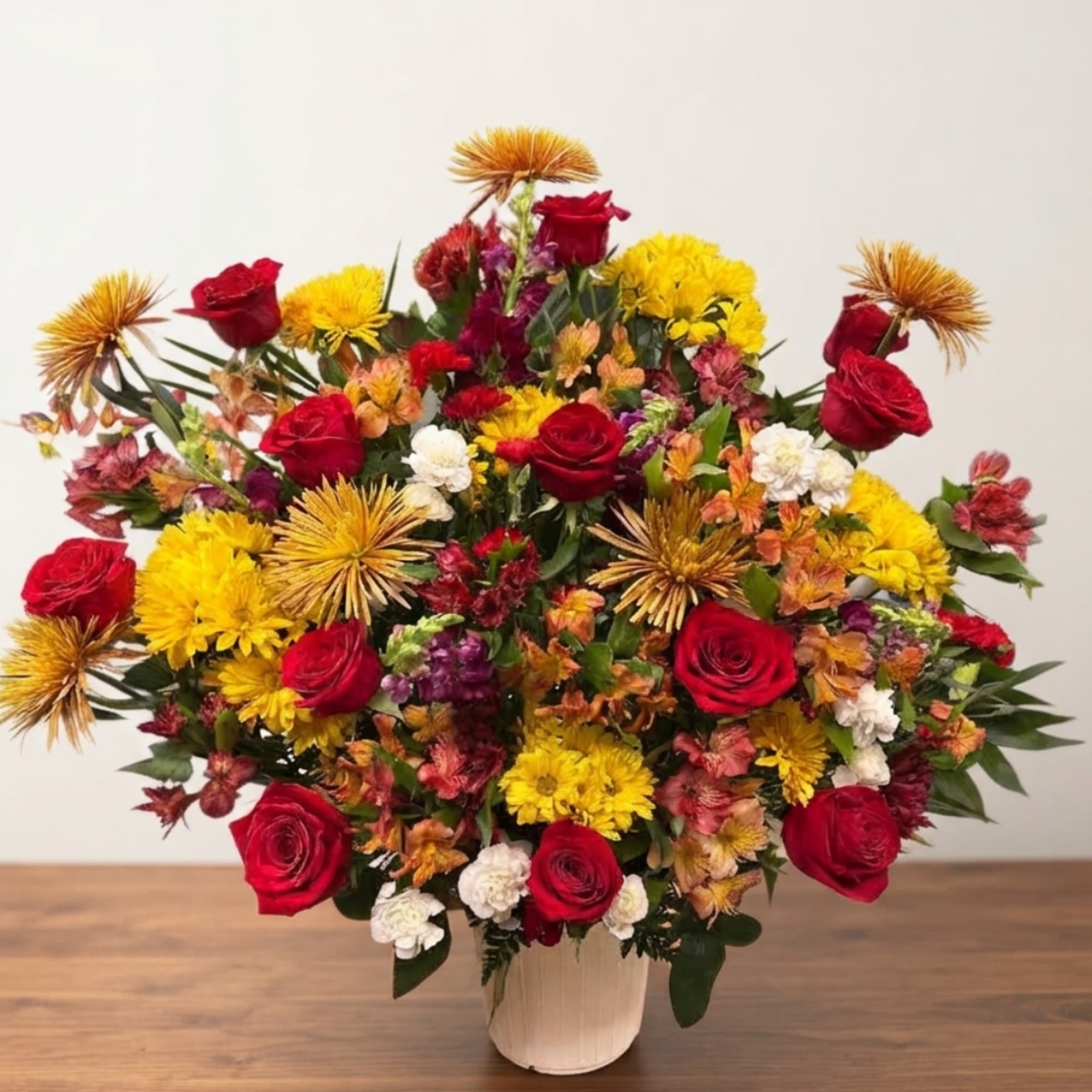 Mixed bouquet of red roses, yellow mums, and orange blooms in a white vase