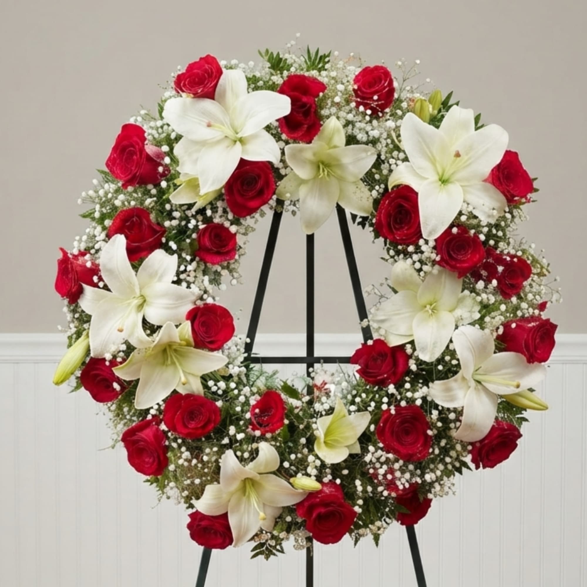 Red roses and white lilies arranged in a circular wreath on a stand