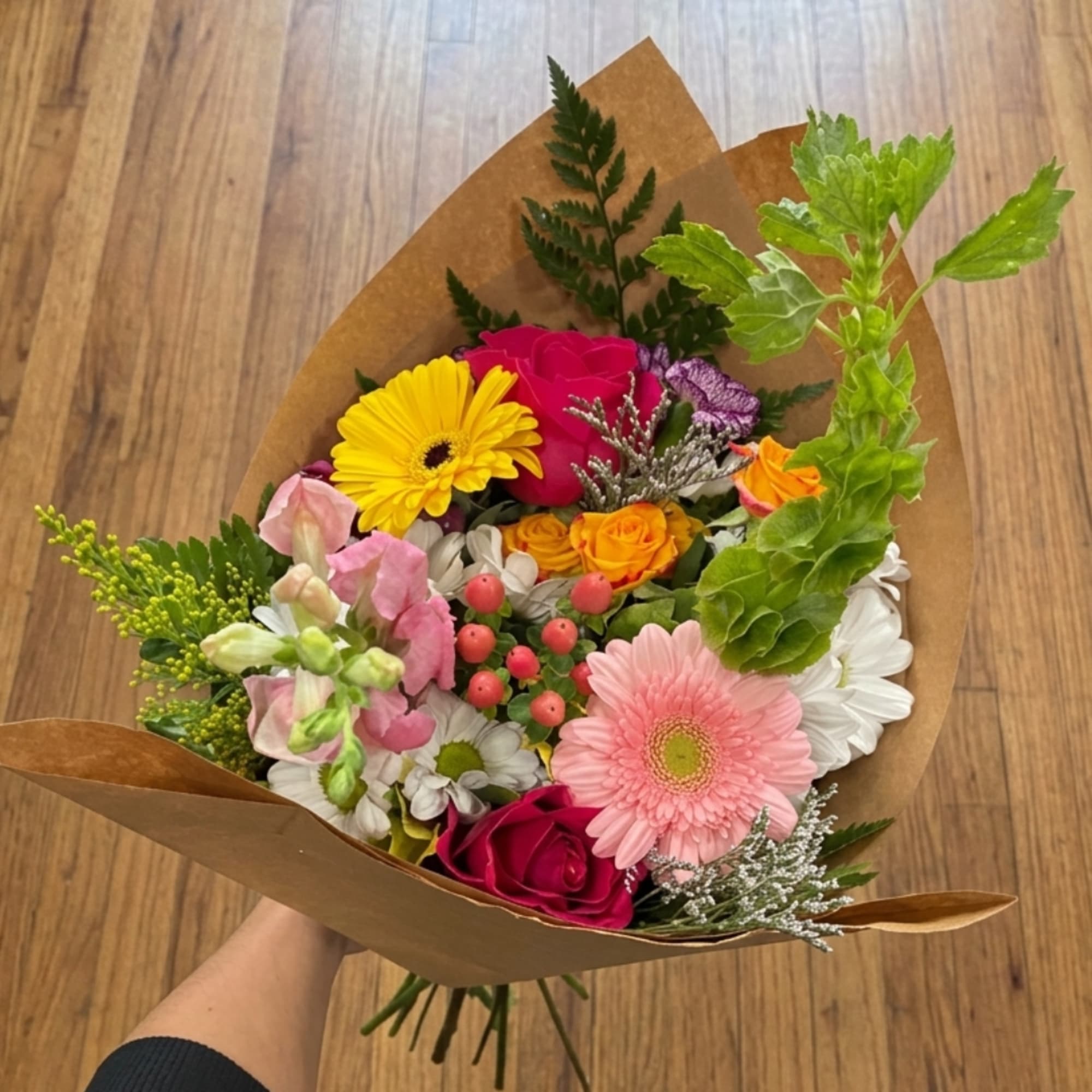 Handheld bouquet with pink, yellow, white, and orange flowers wrapped in brown paper
