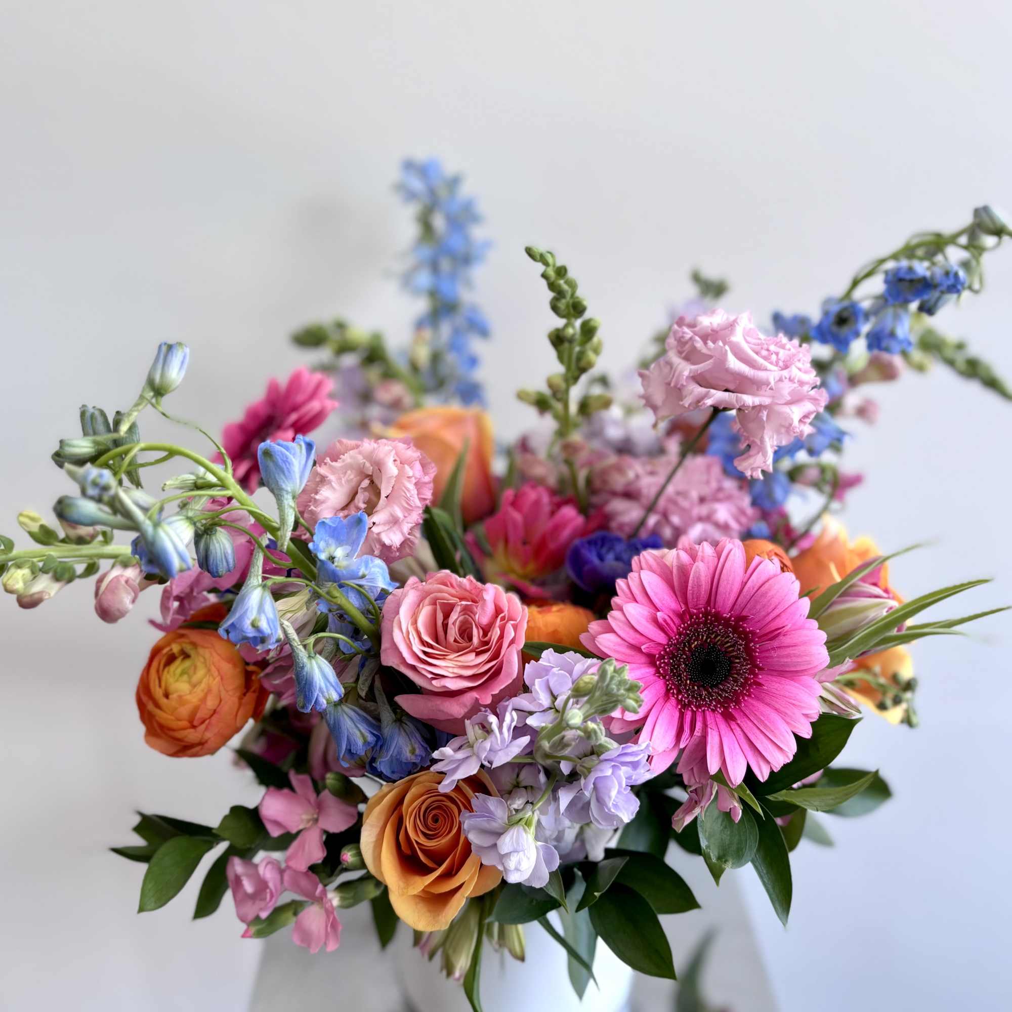 Colorful mixed bouquet in a white vase with pink, orange, blue, and purple blooms