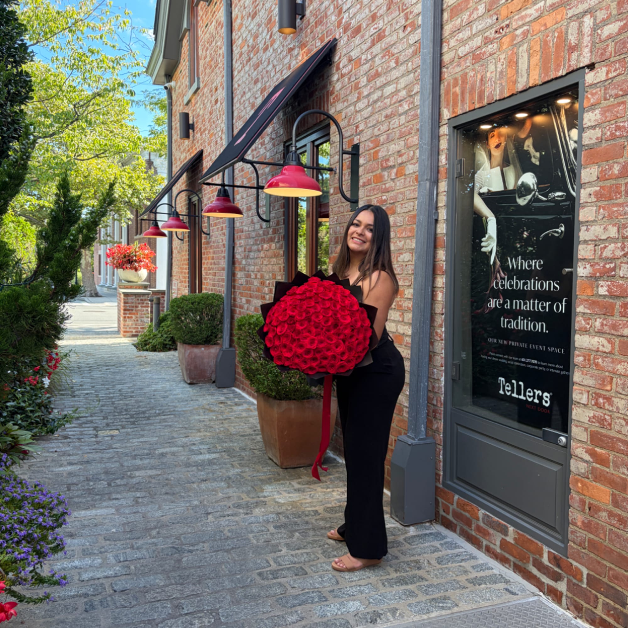 Woman holding a large bouquet of red roses outside a brick building