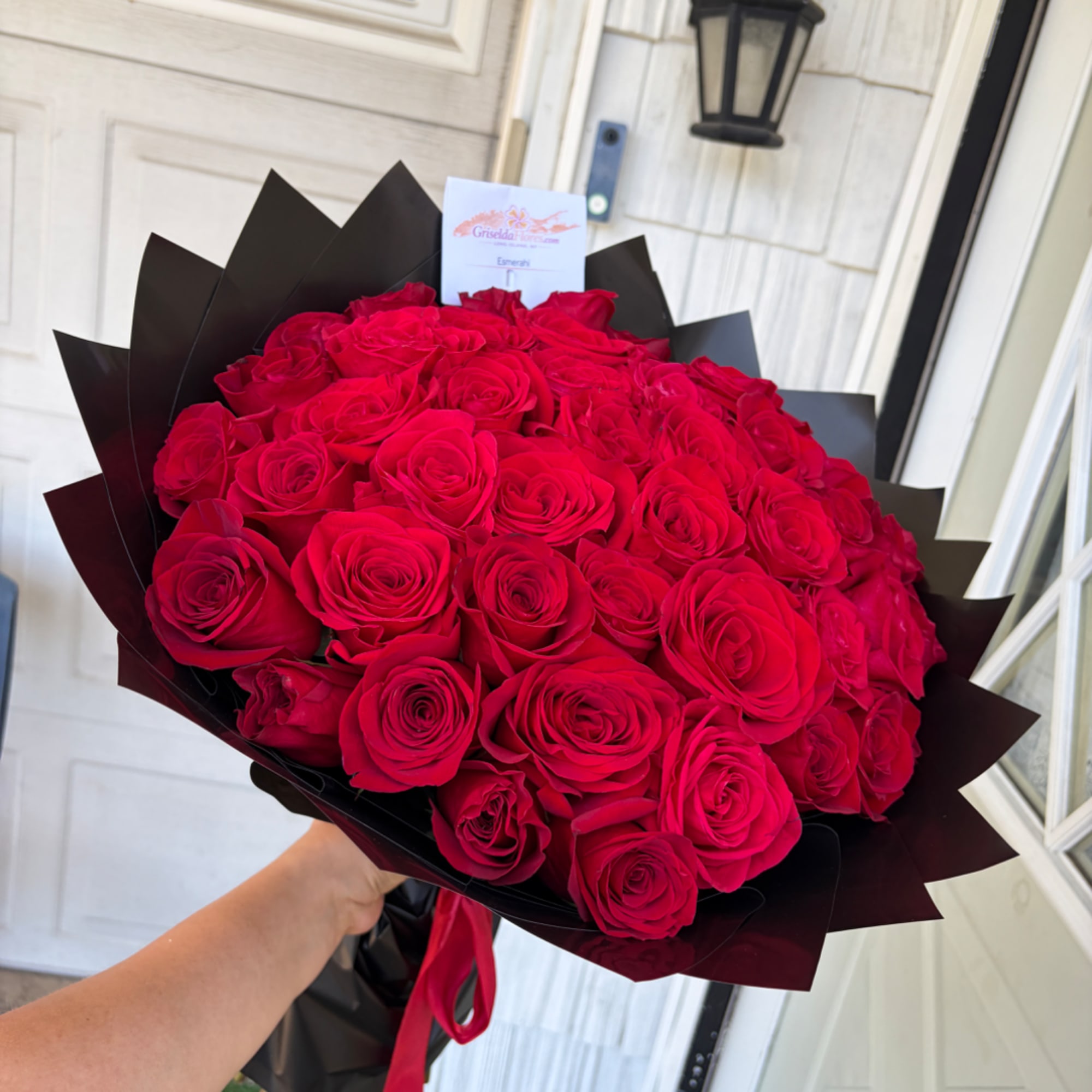 Large bouquet of red roses wrapped in black paper and tied with a red ribbon