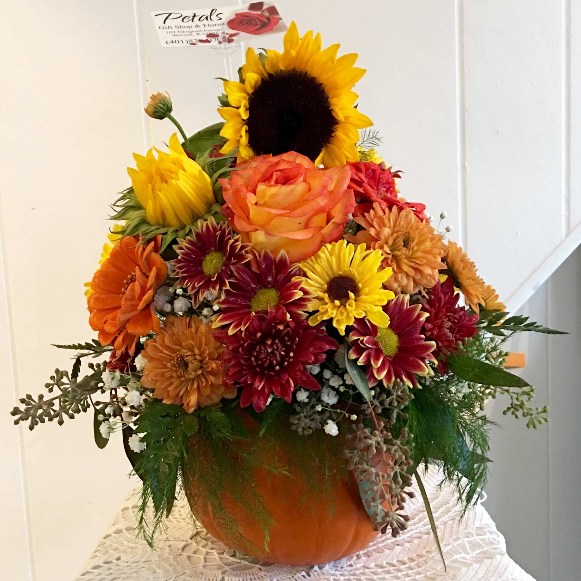 Mixed autumn bouquet in an orange pumpkin vase with sunflowers and roses