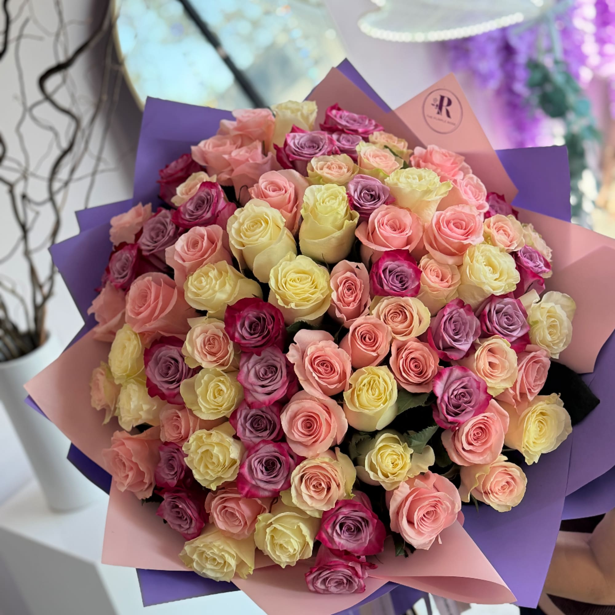 Large bouquet of pink, lavender, and yellow roses wrapped in purple and pink paper