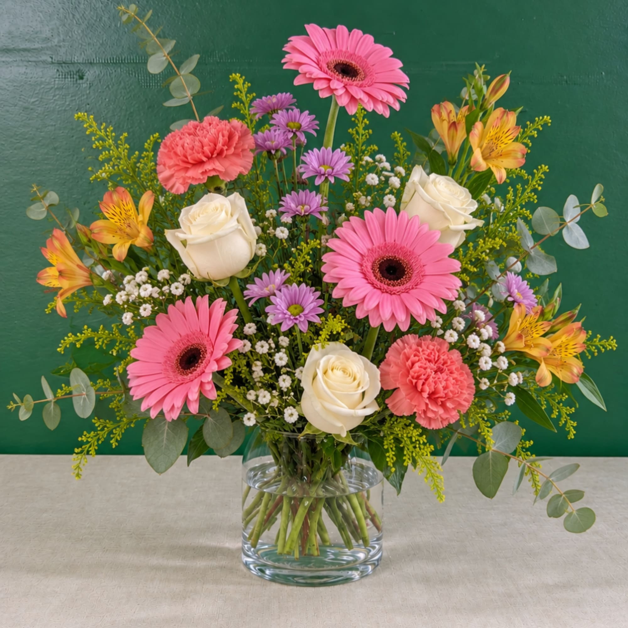 Pink gerberas, white roses, and purple daisies in a glass vase