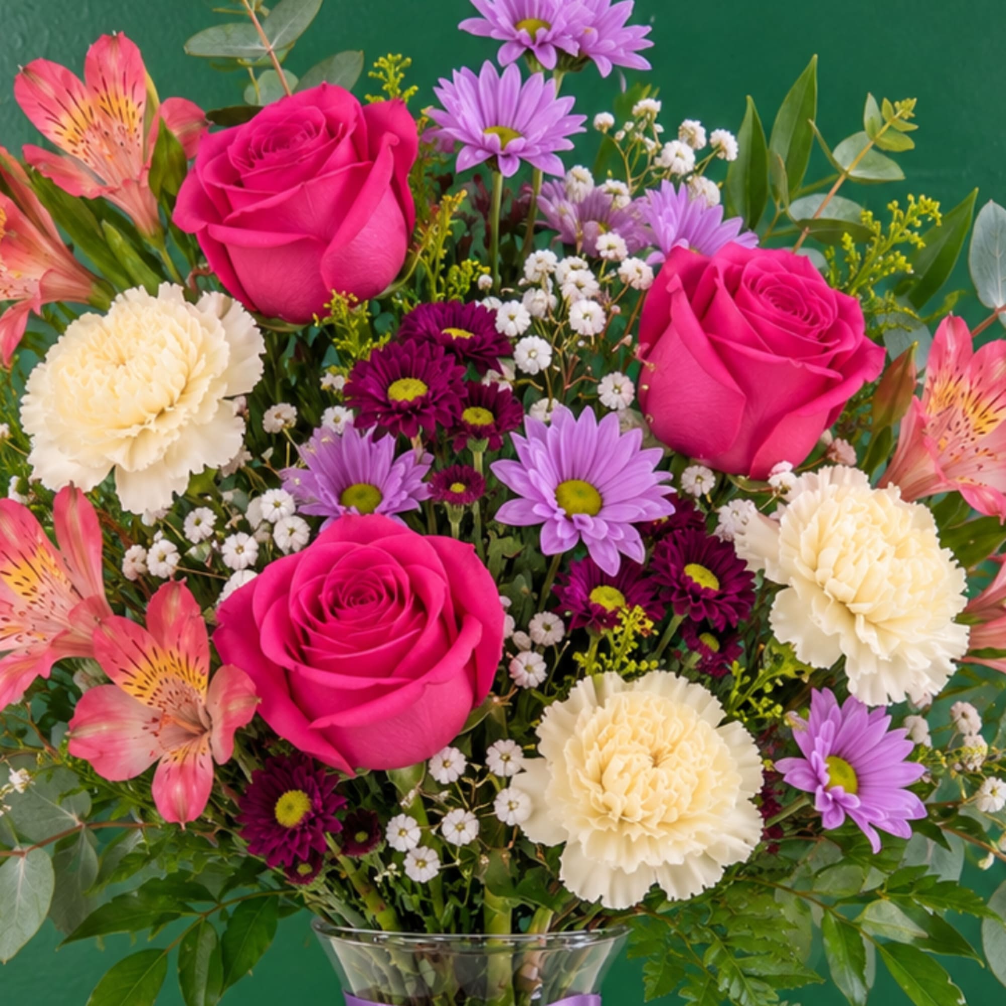 Bouquet of pink roses, purple daisies, and cream carnations in a glass vase