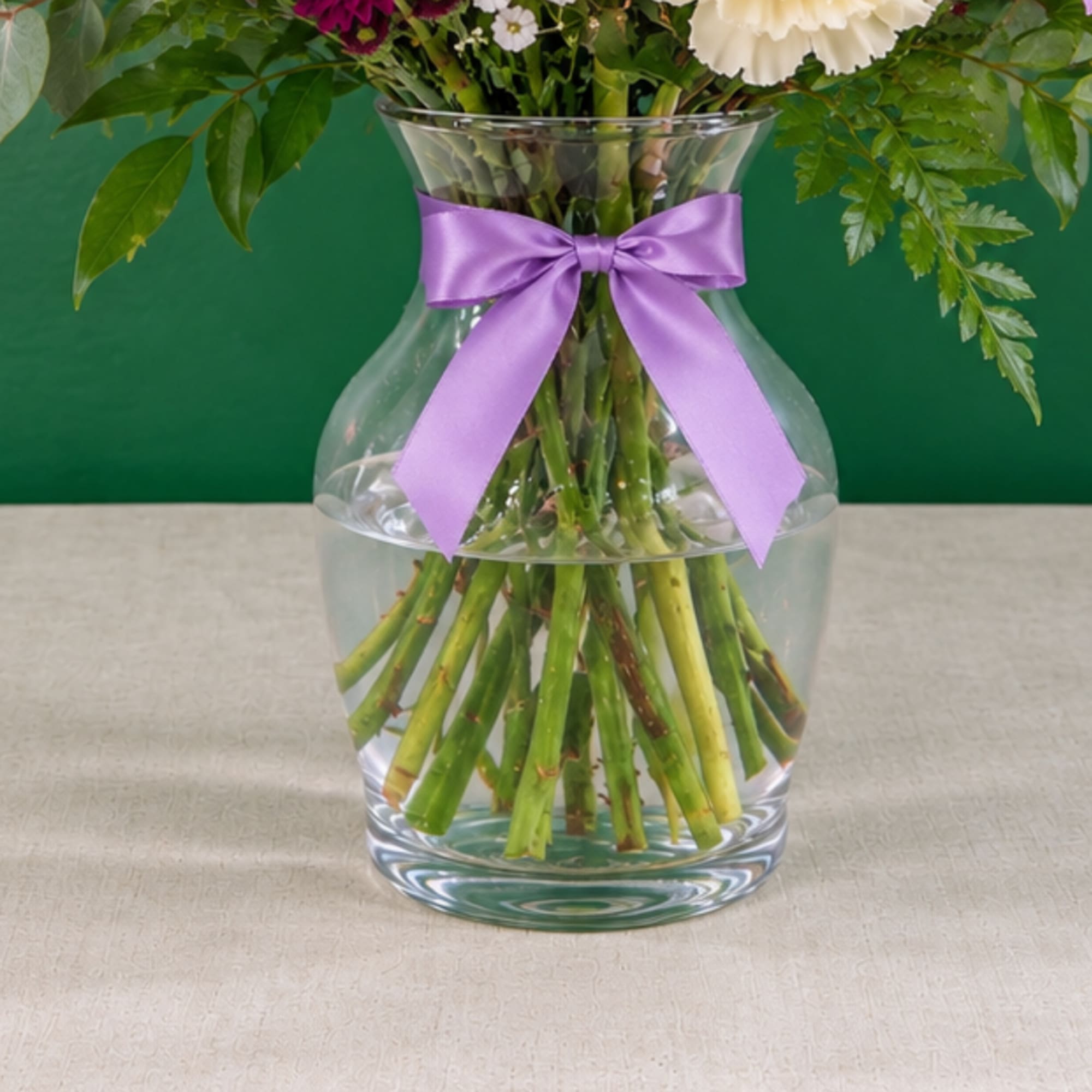 White flowers in a clear glass vase with a purple ribbon