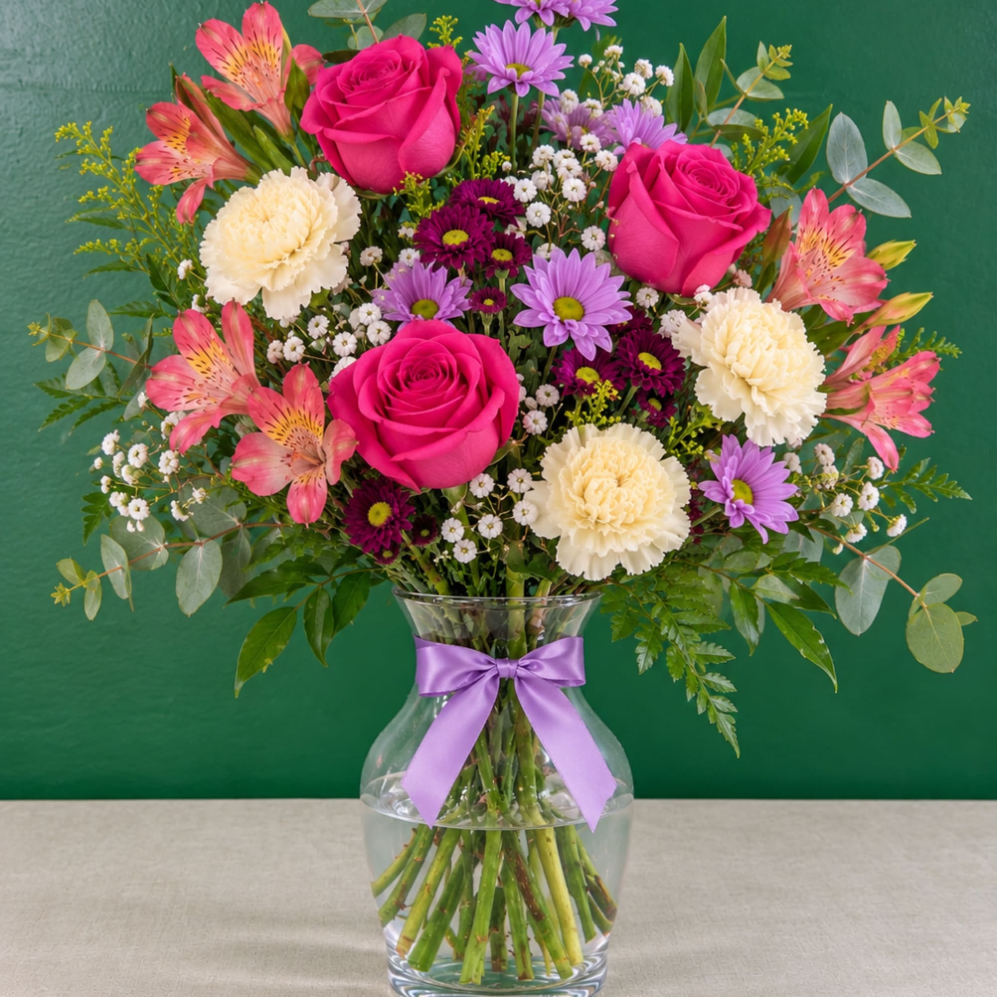 Pink roses and mixed flowers in a glass vase with a purple ribbon