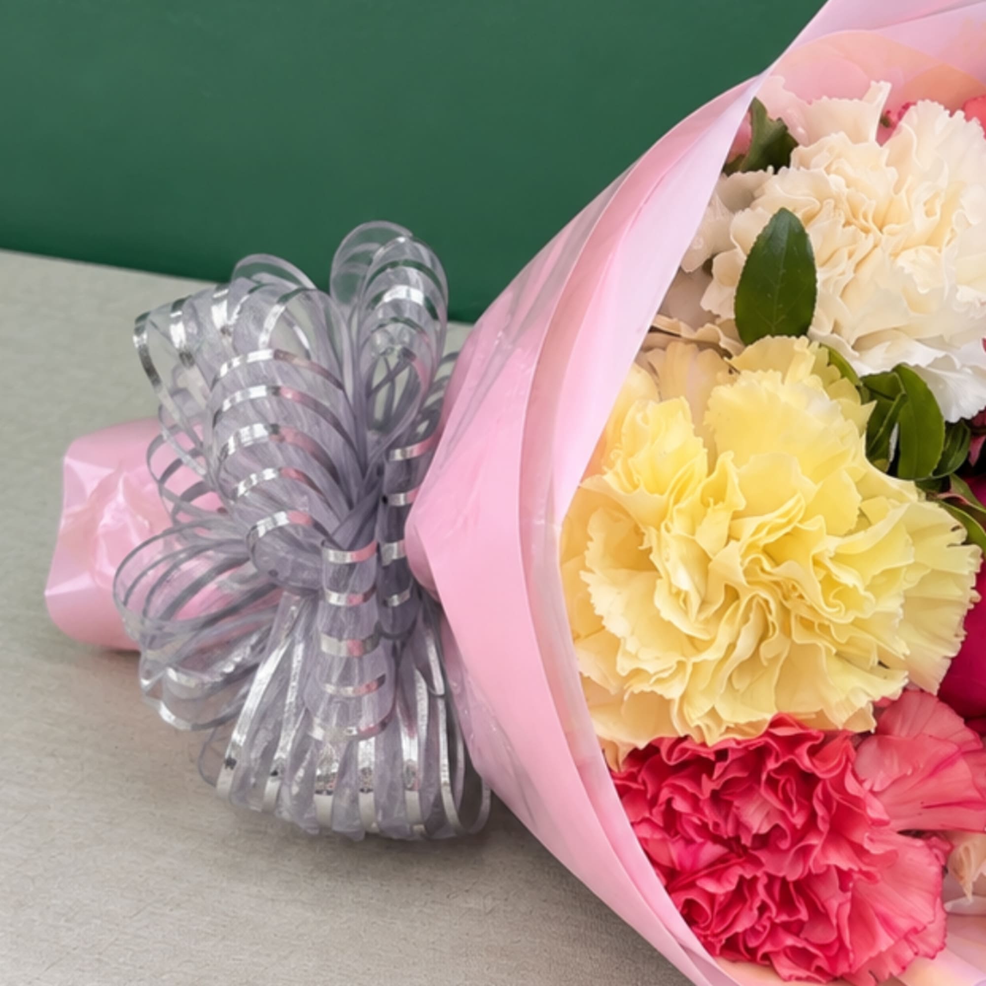 Bouquet of pink, yellow, and white carnations wrapped in pink paper