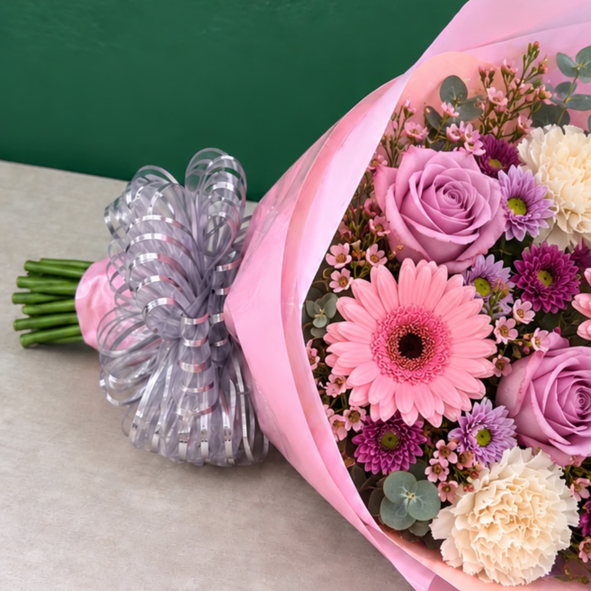 Pink and purple bouquet wrapped in pink paper with a silver ribbon bow