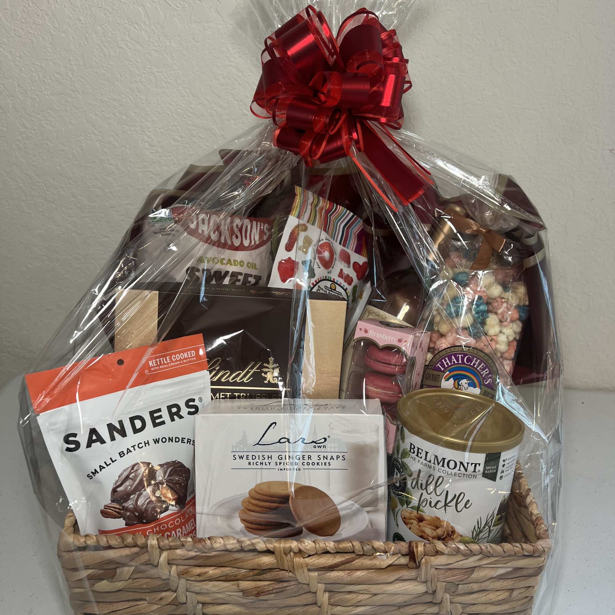 Gift basket of assorted snacks and sweets wrapped in clear cellophane with a red bow