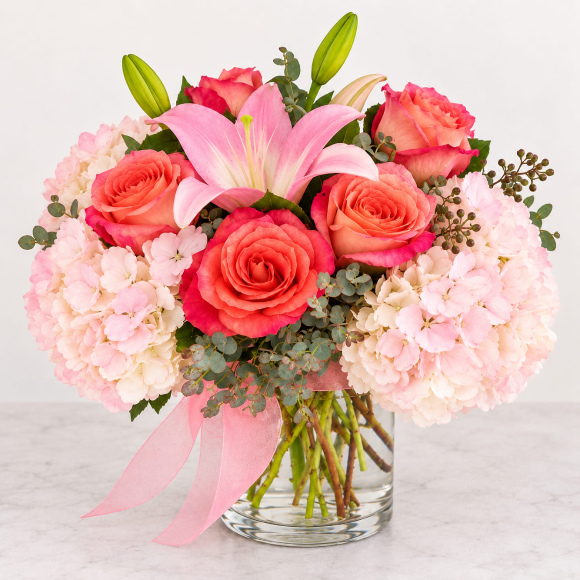 Pink lilies and coral roses in a clear glass vase with hydrangeas
