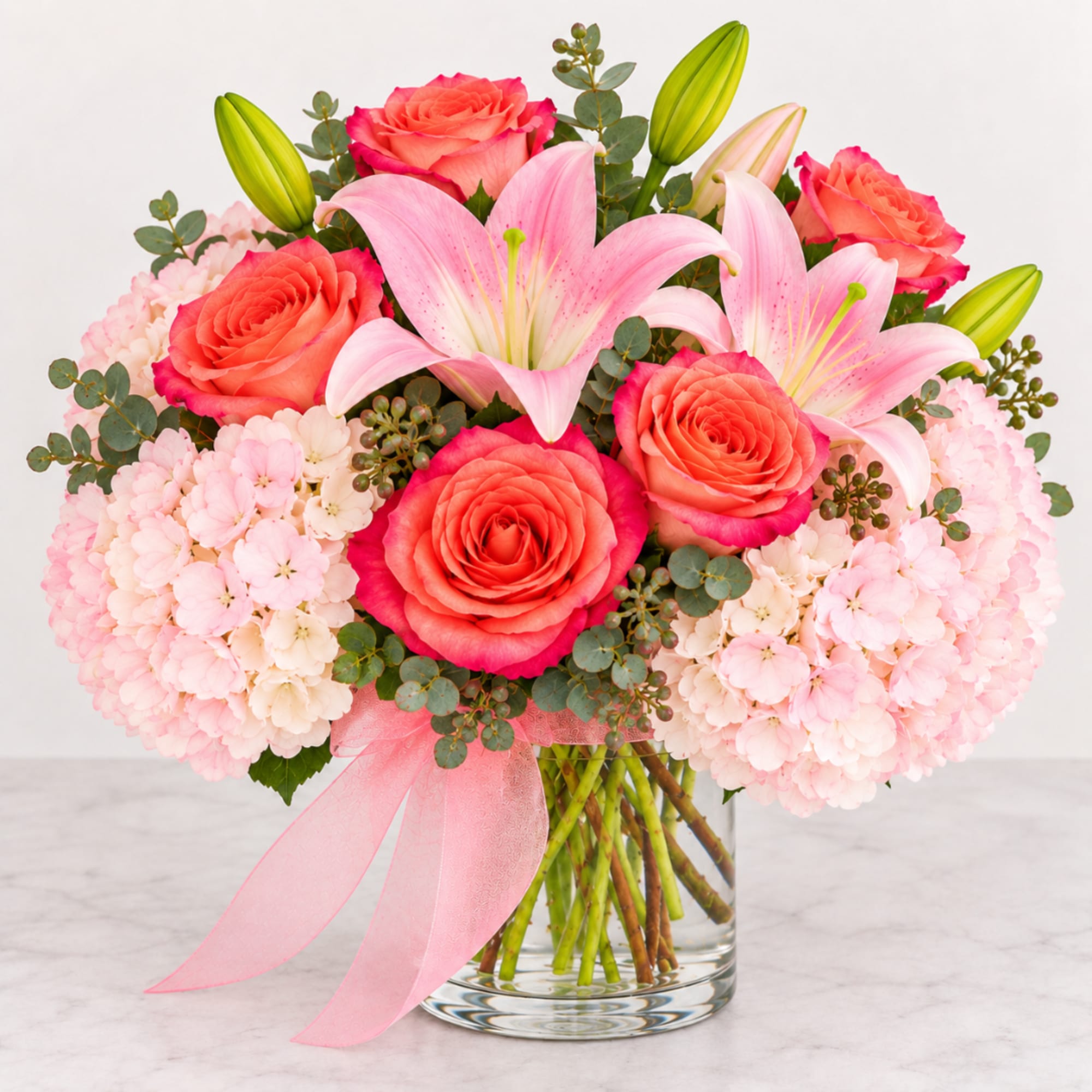 Pink roses and lilies arranged in a clear glass vase with a pink ribbon