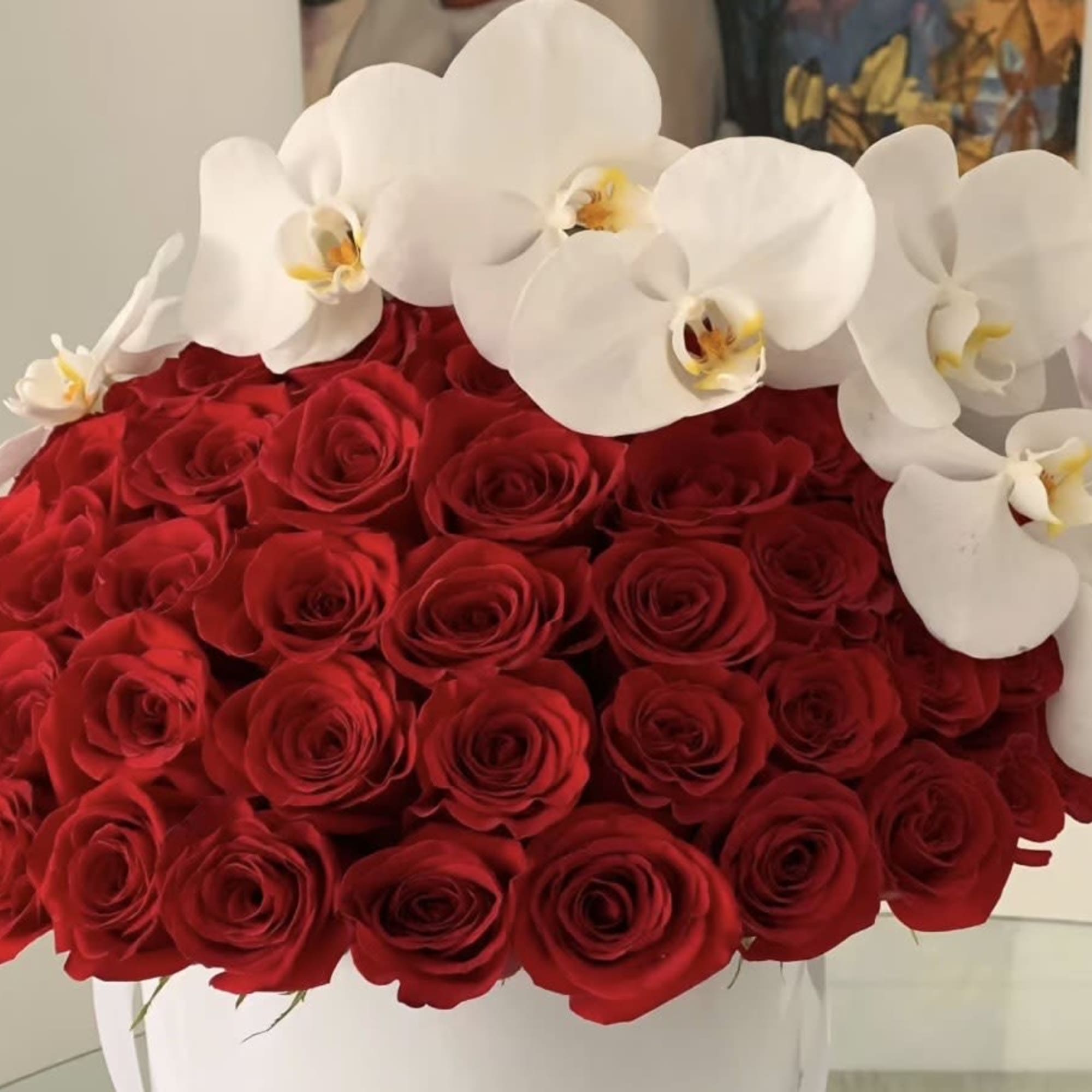 Low arrangement of red roses topped with white orchids in a white container