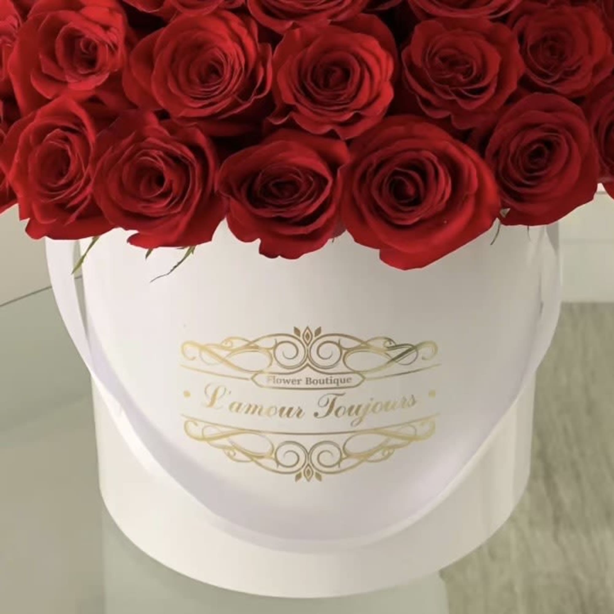 Dense arrangement of red roses in a round white hat box with gold script on the front