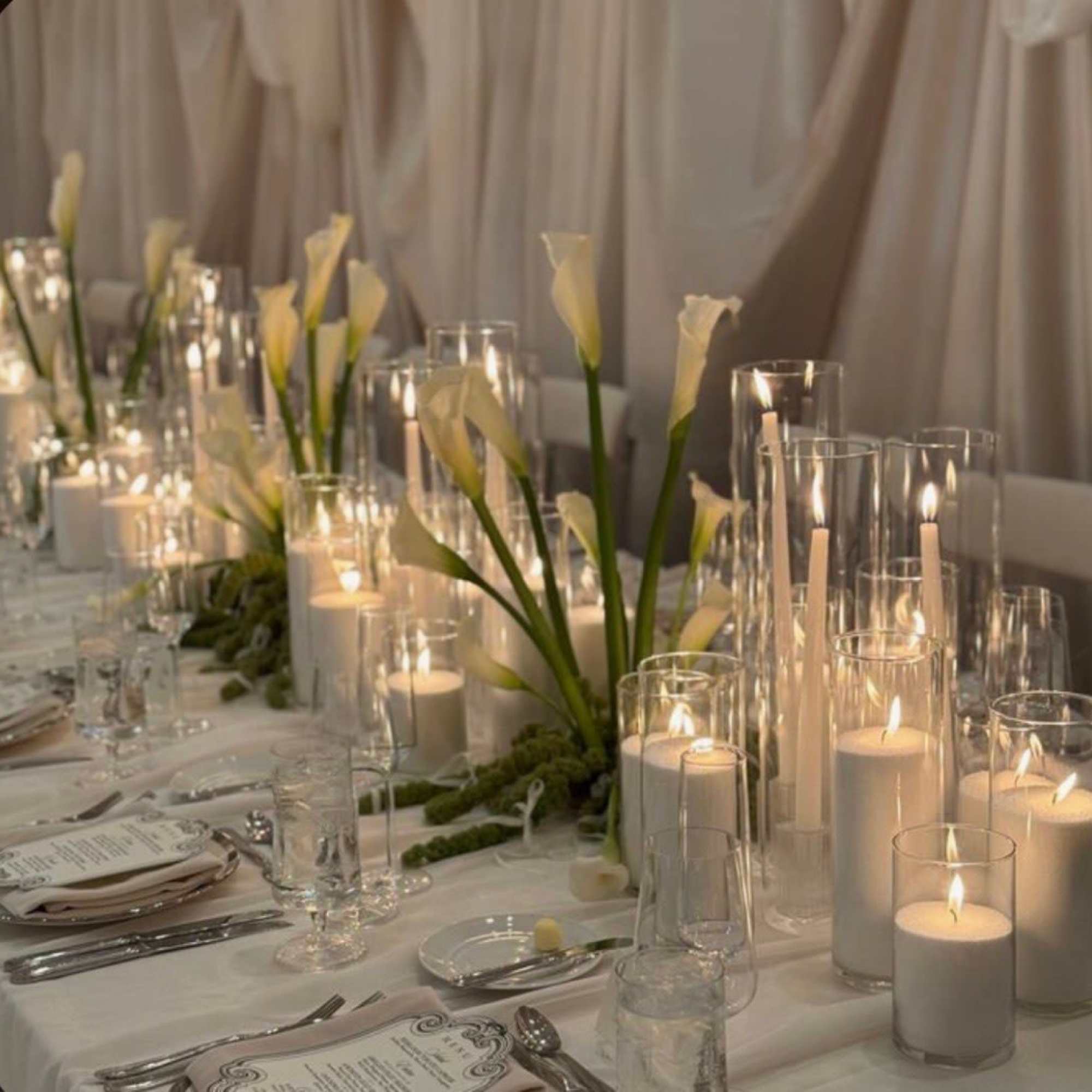 White calla lilies and candles in glass cylinders on a banquet table