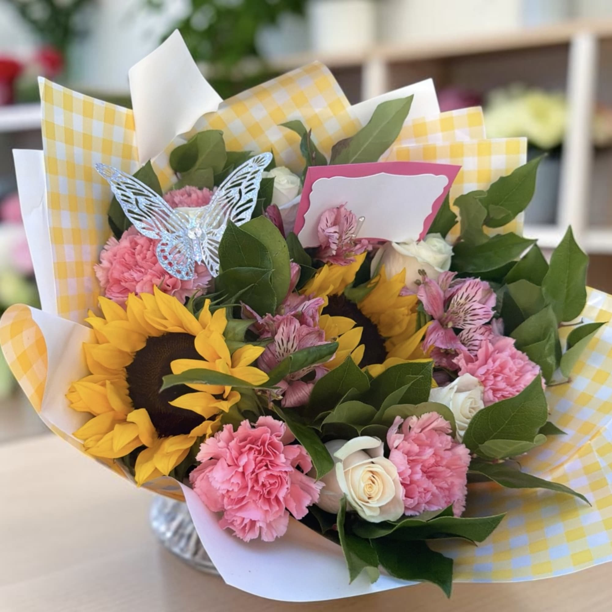 Bouquet of sunflowers, pink carnations, and white roses in yellow checkered wrap