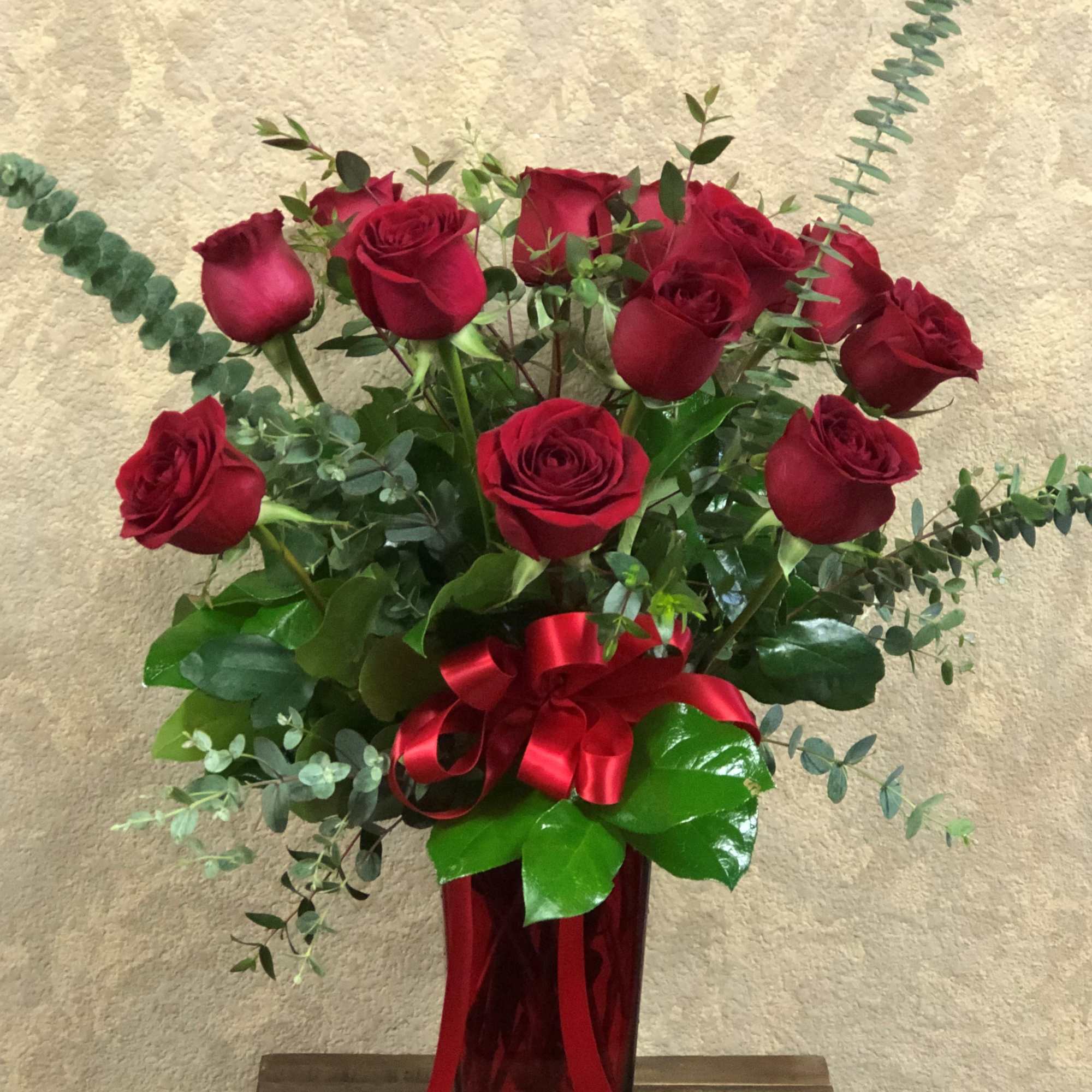 Tall arrangement of red roses with eucalyptus in a red glass vase with a red bow