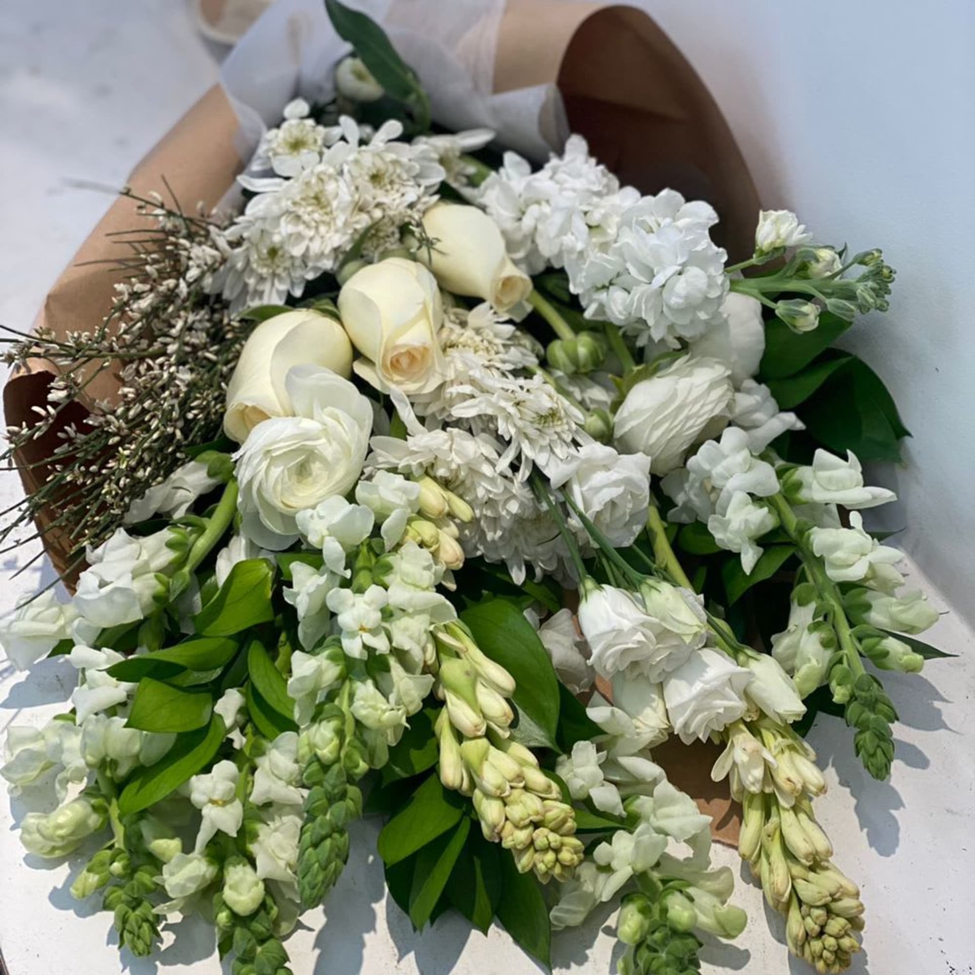 White bouquet with roses and mixed blooms wrapped in brown paper