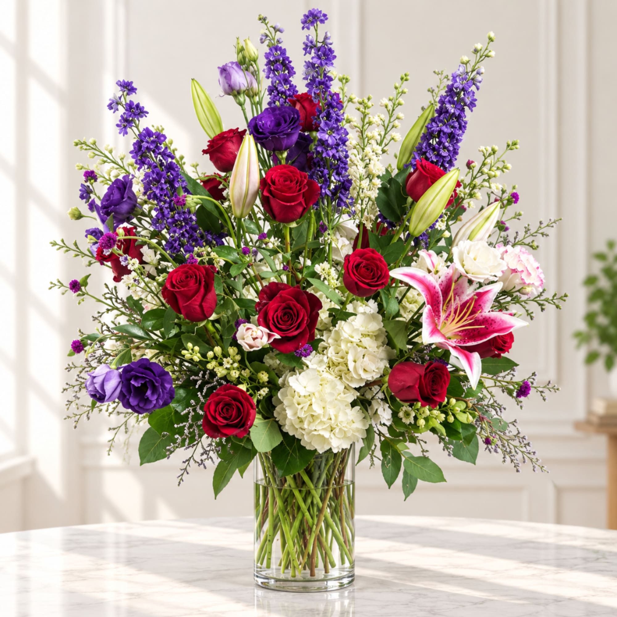 Tall bouquet of red roses, purple blooms, white hydrangea, and lilies in a glass vase
