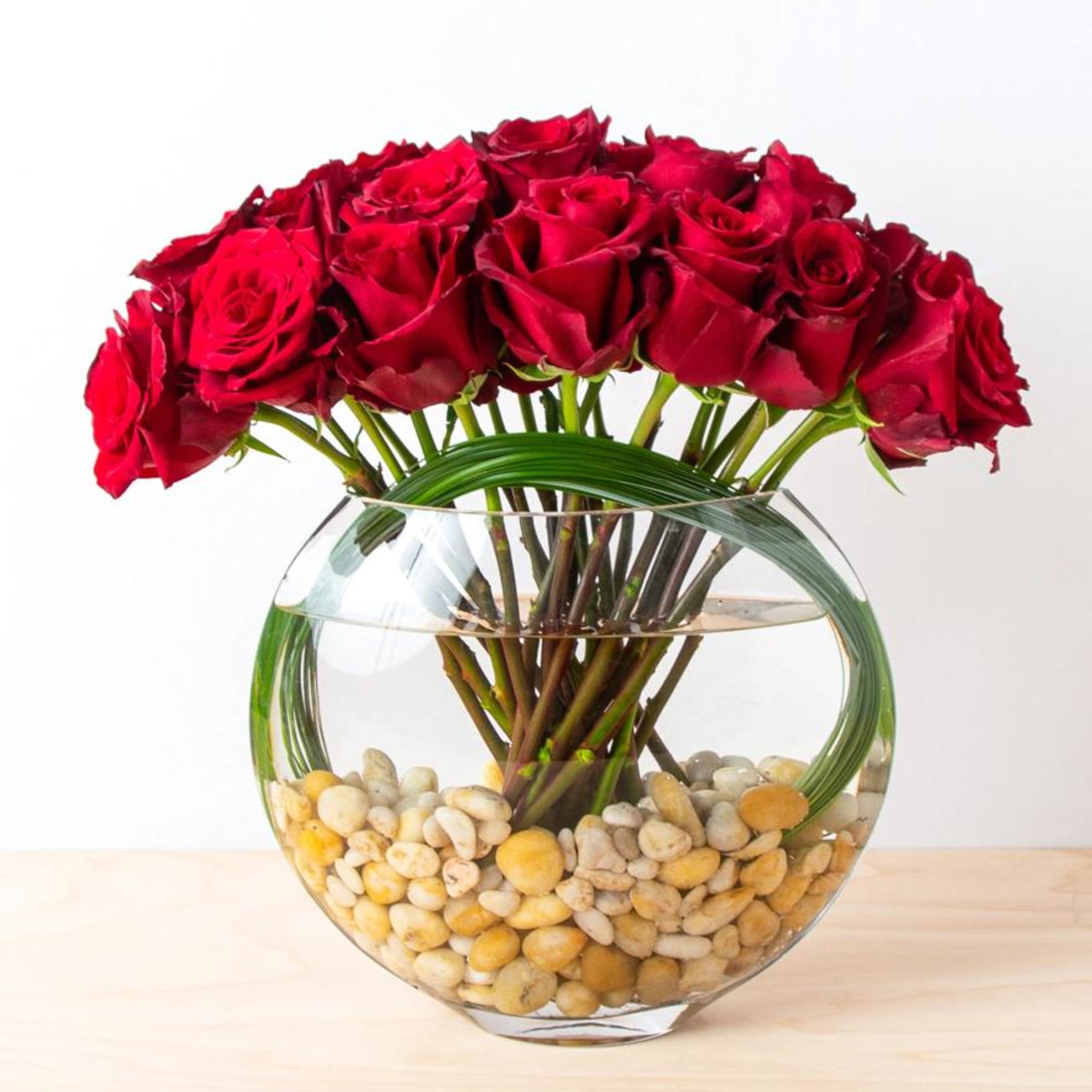 Red roses arranged in a round glass vase with pebbles