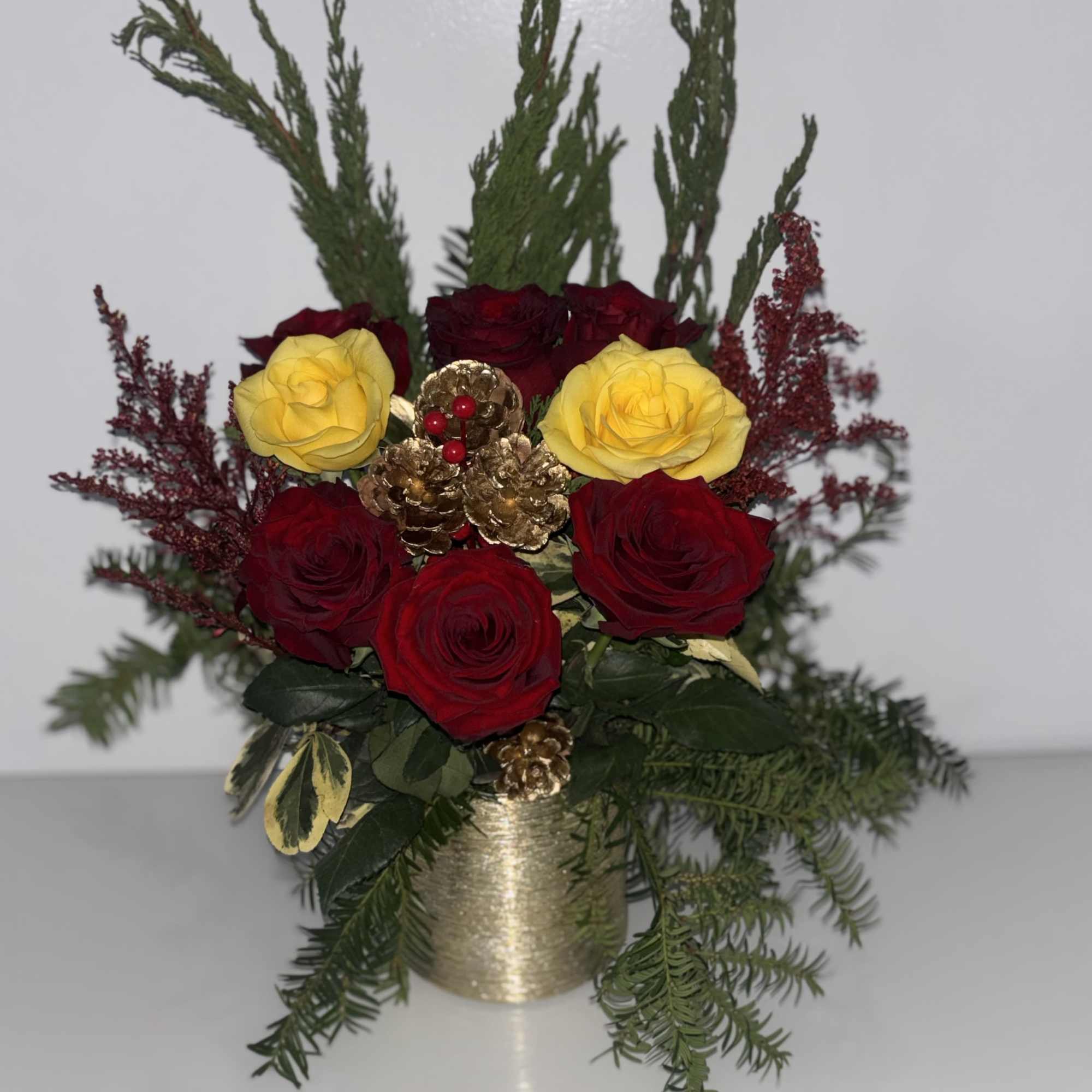 Red and yellow roses in a gold vase with evergreen accents