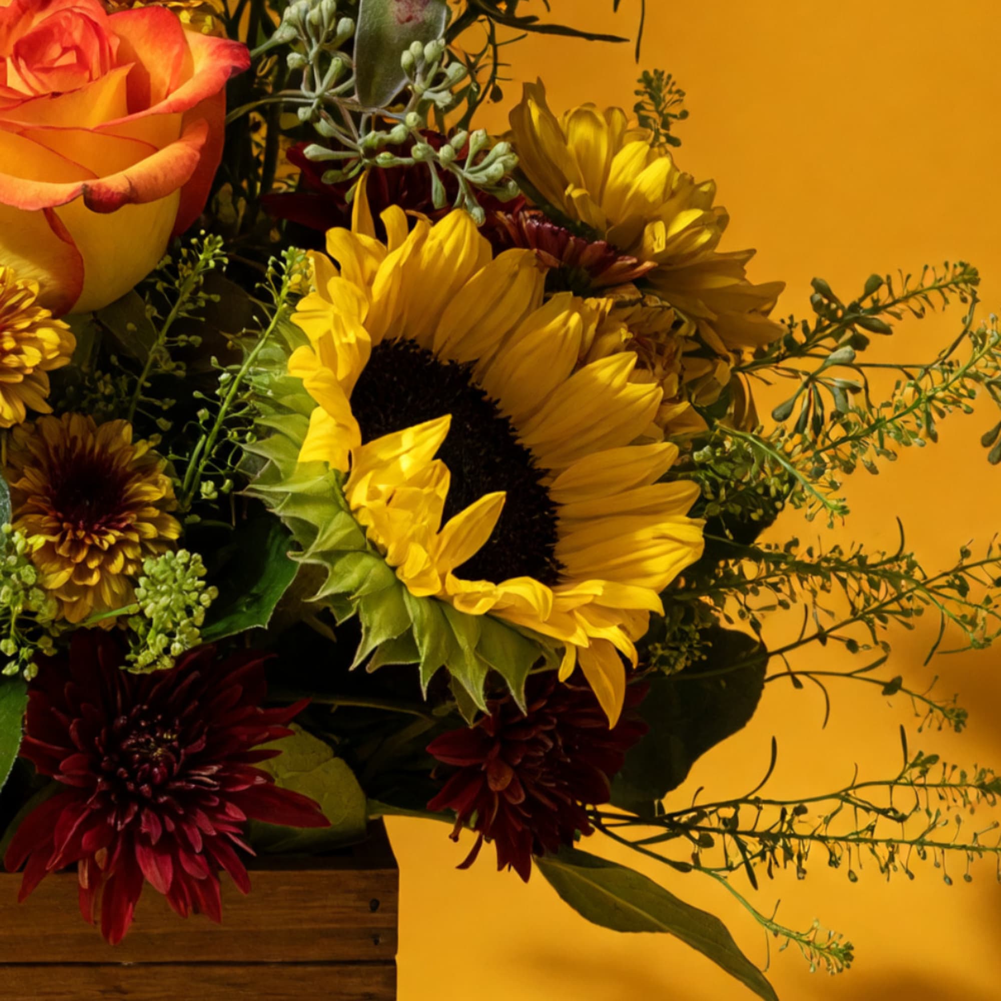 Sunflower and rose bouquet with burgundy chrysanthemums in a wooden box