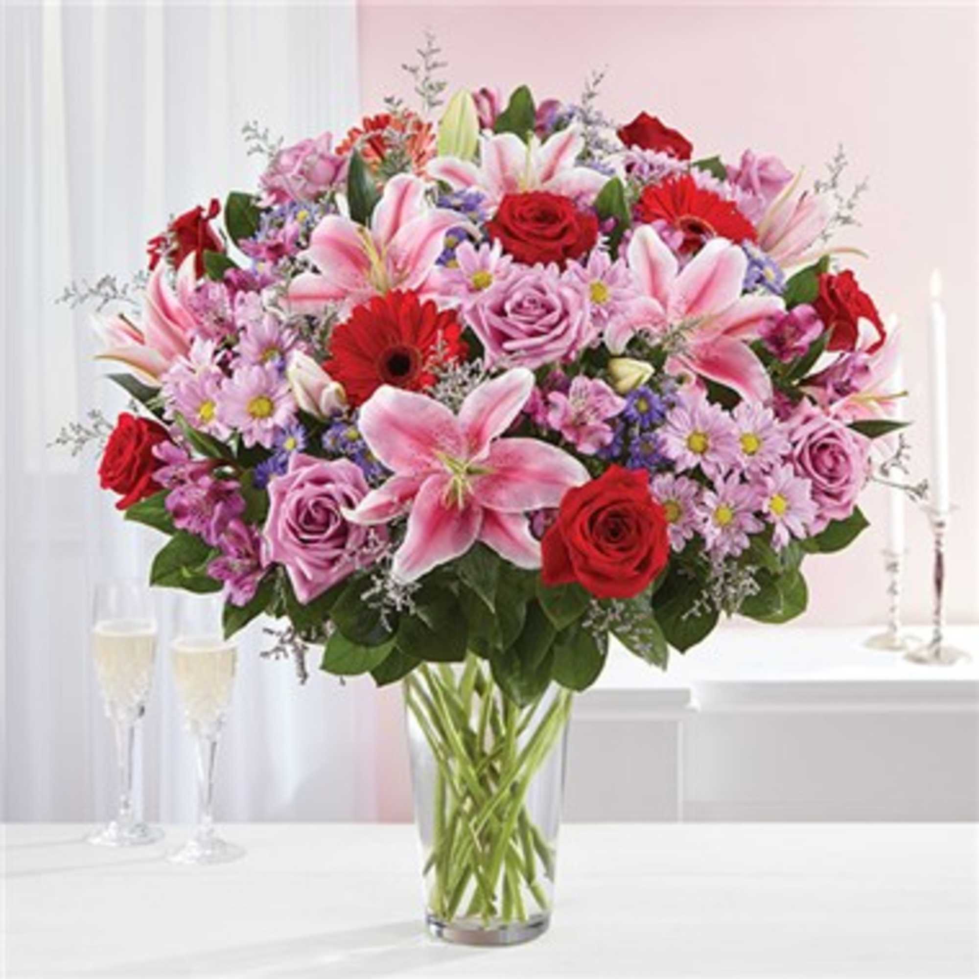 Mixed bouquet of pink lilies, red roses, and lavender flowers in a glass vase