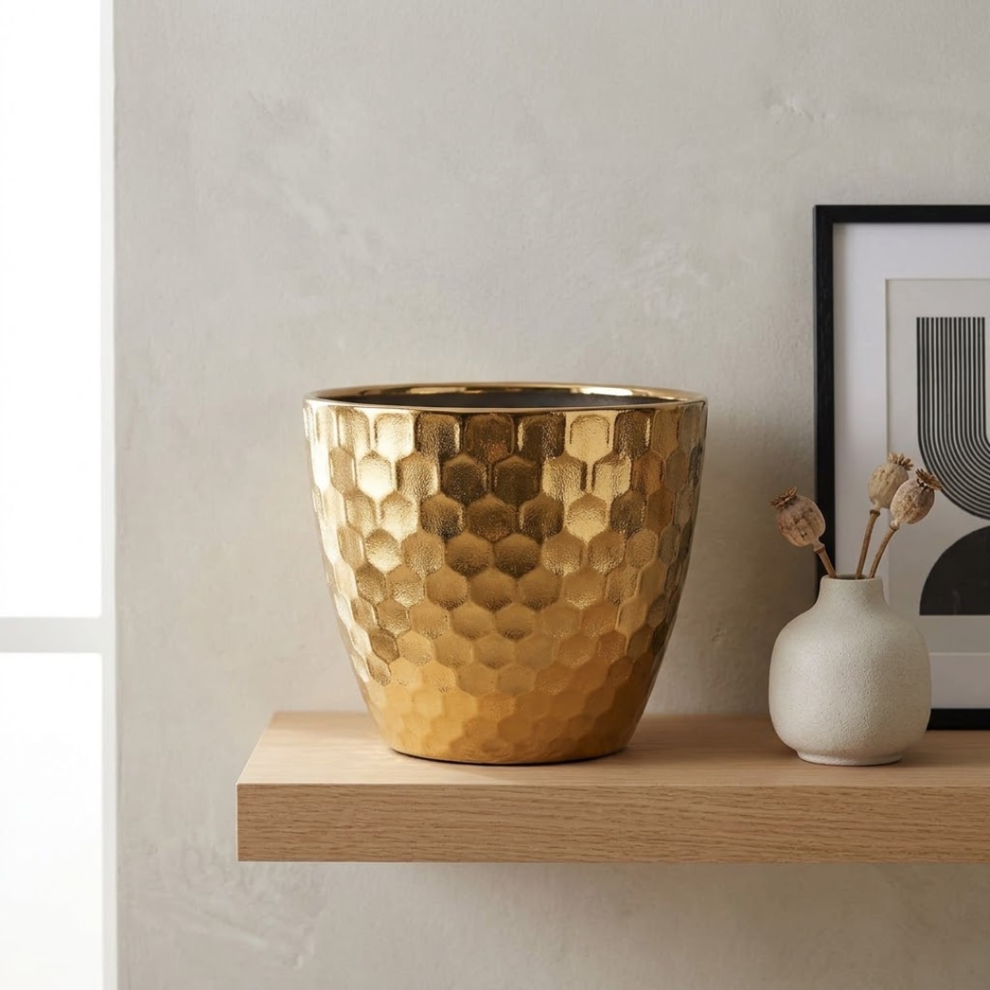 Gold hammered planter on a wooden shelf beside a small white vase