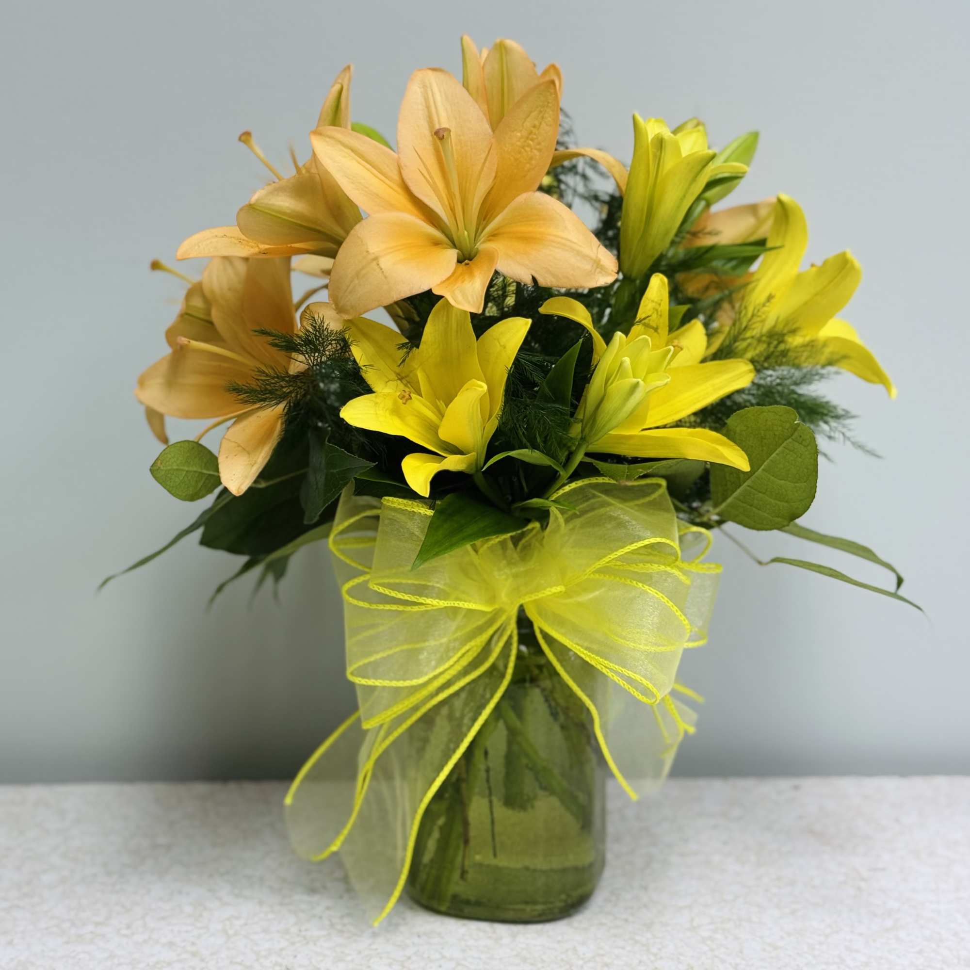 Yellow and peach lilies arranged in a glass vase with a ribbon bow.