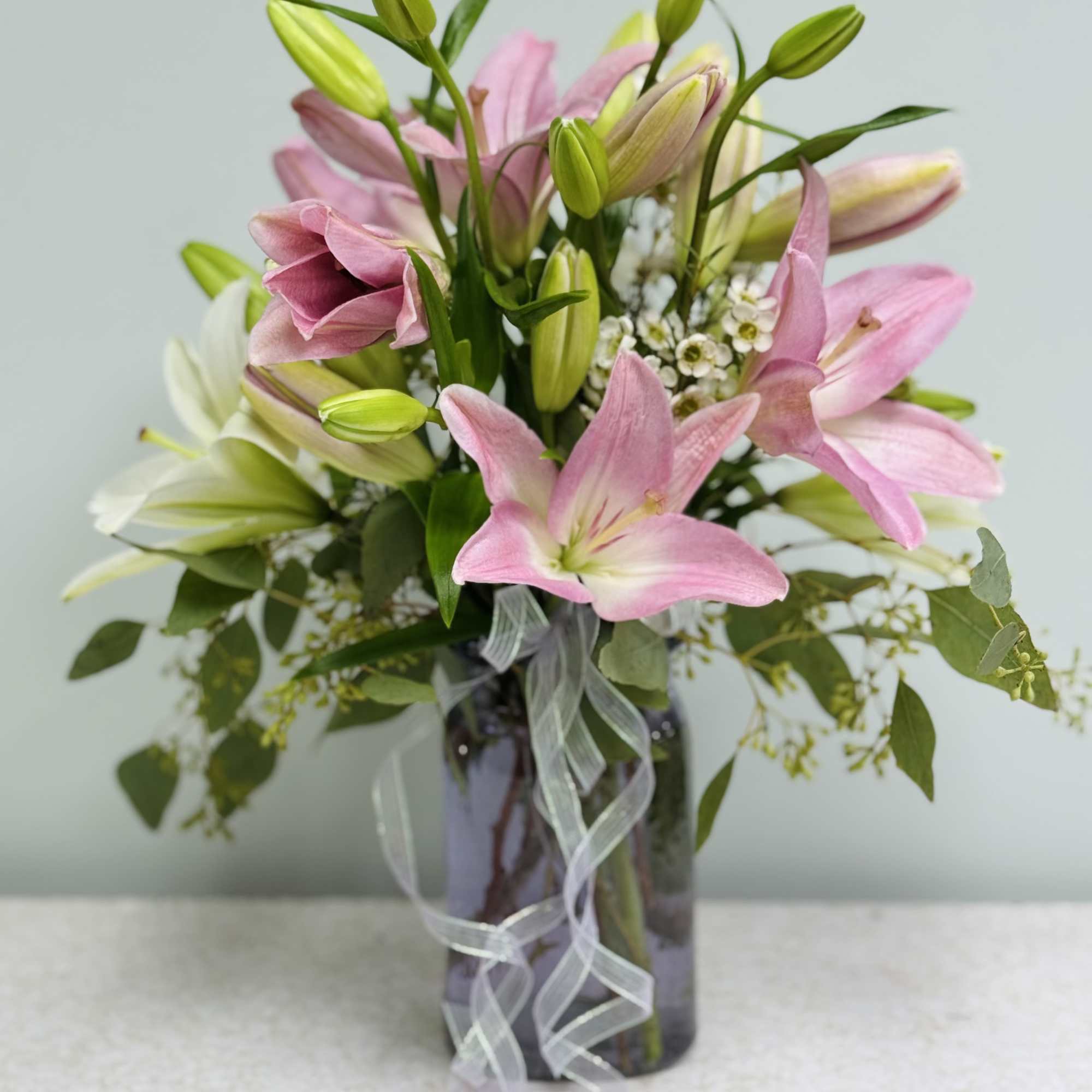 Pink and white lilies in a glass vase with a ribbon