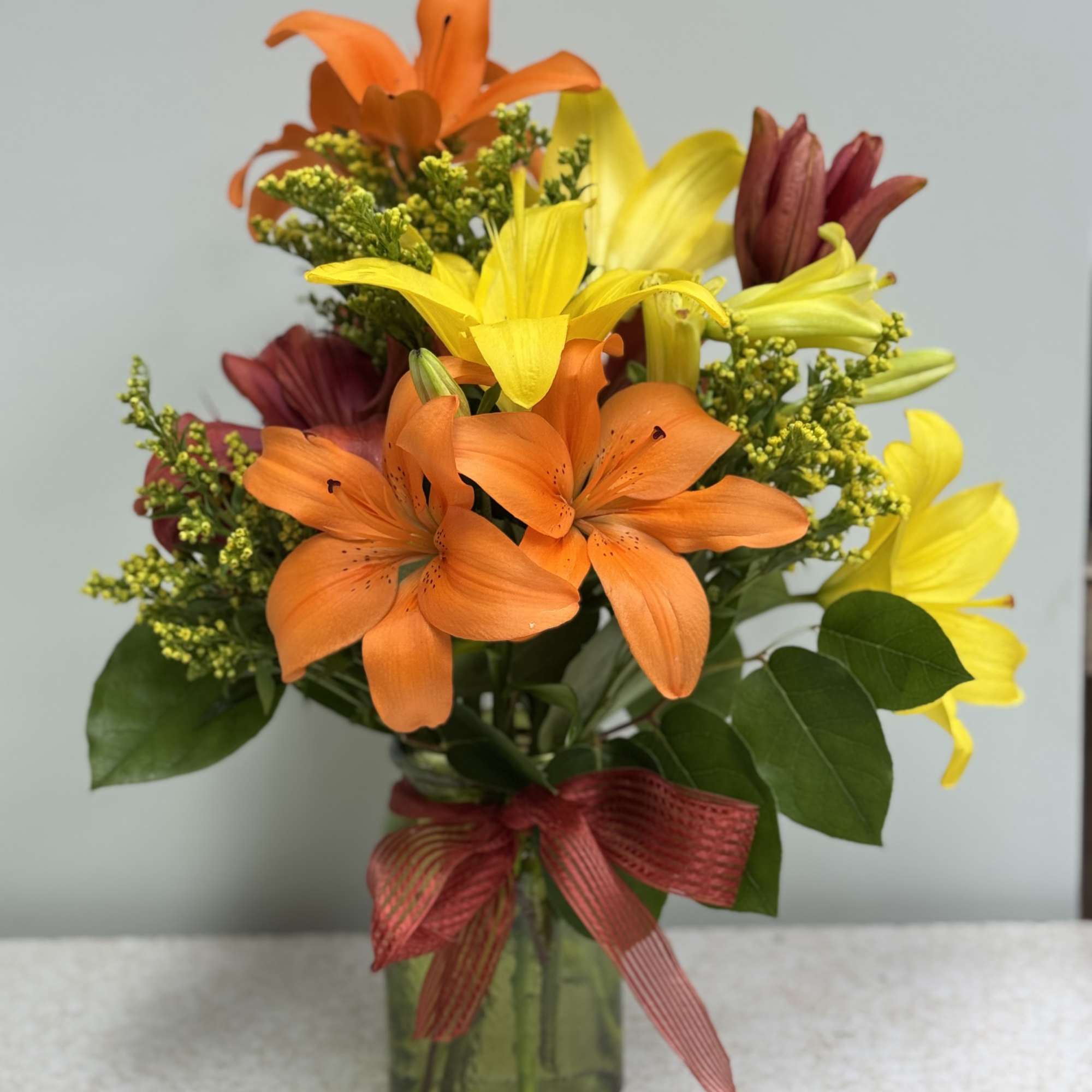 Orange and yellow lilies in a glass vase with a red ribbon