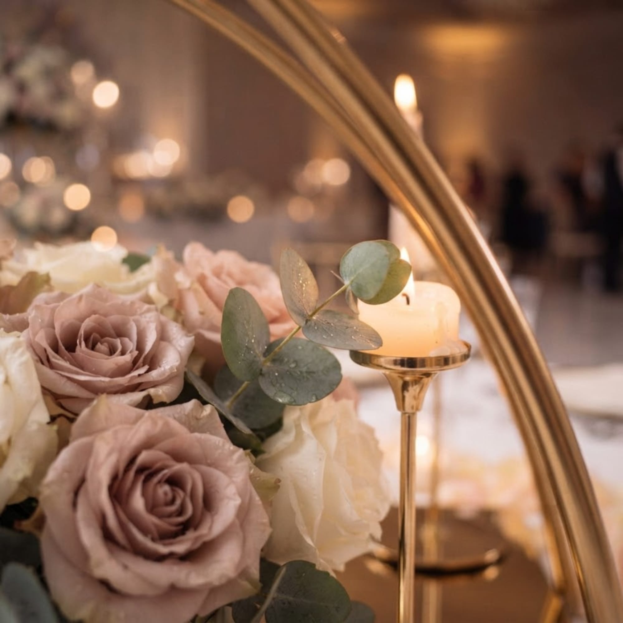 Blush and white roses arranged beside a lit candle on a gold stand