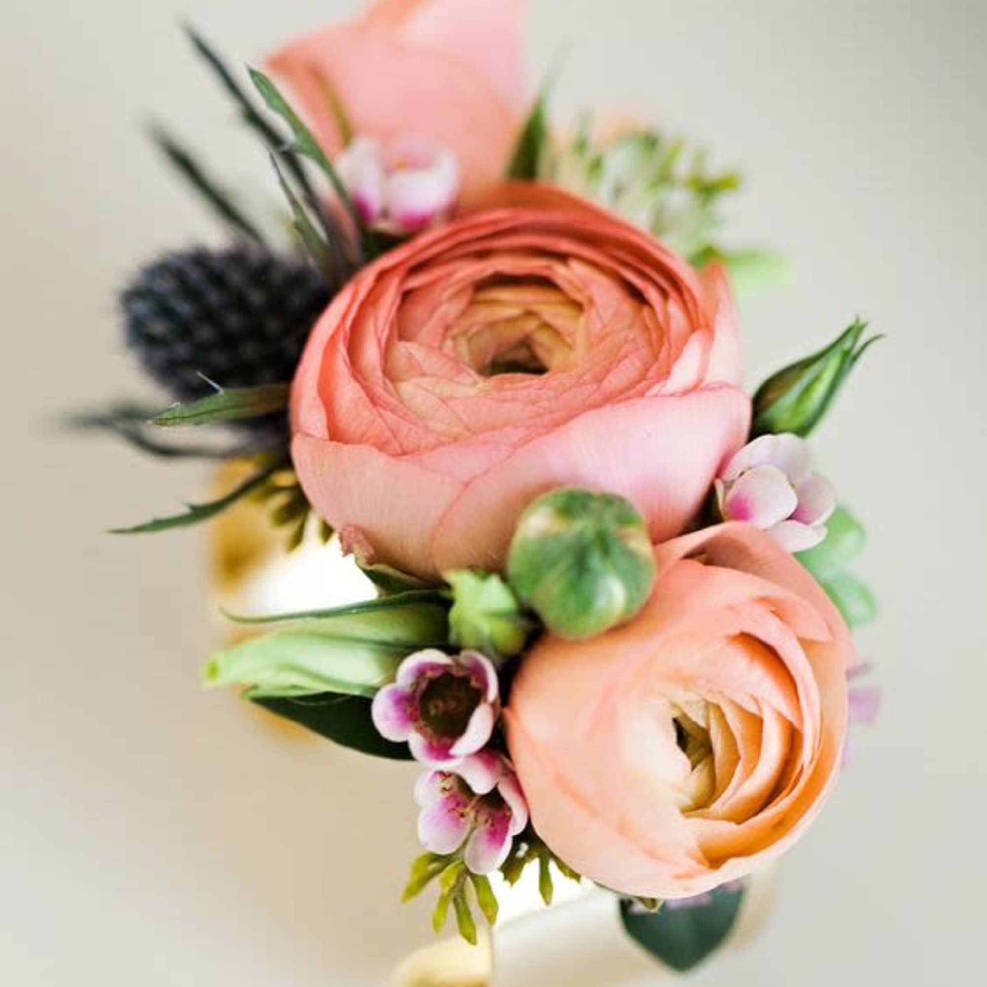 Peach ranunculus wrist corsage with small pink blossoms on a gold cuff bracelet