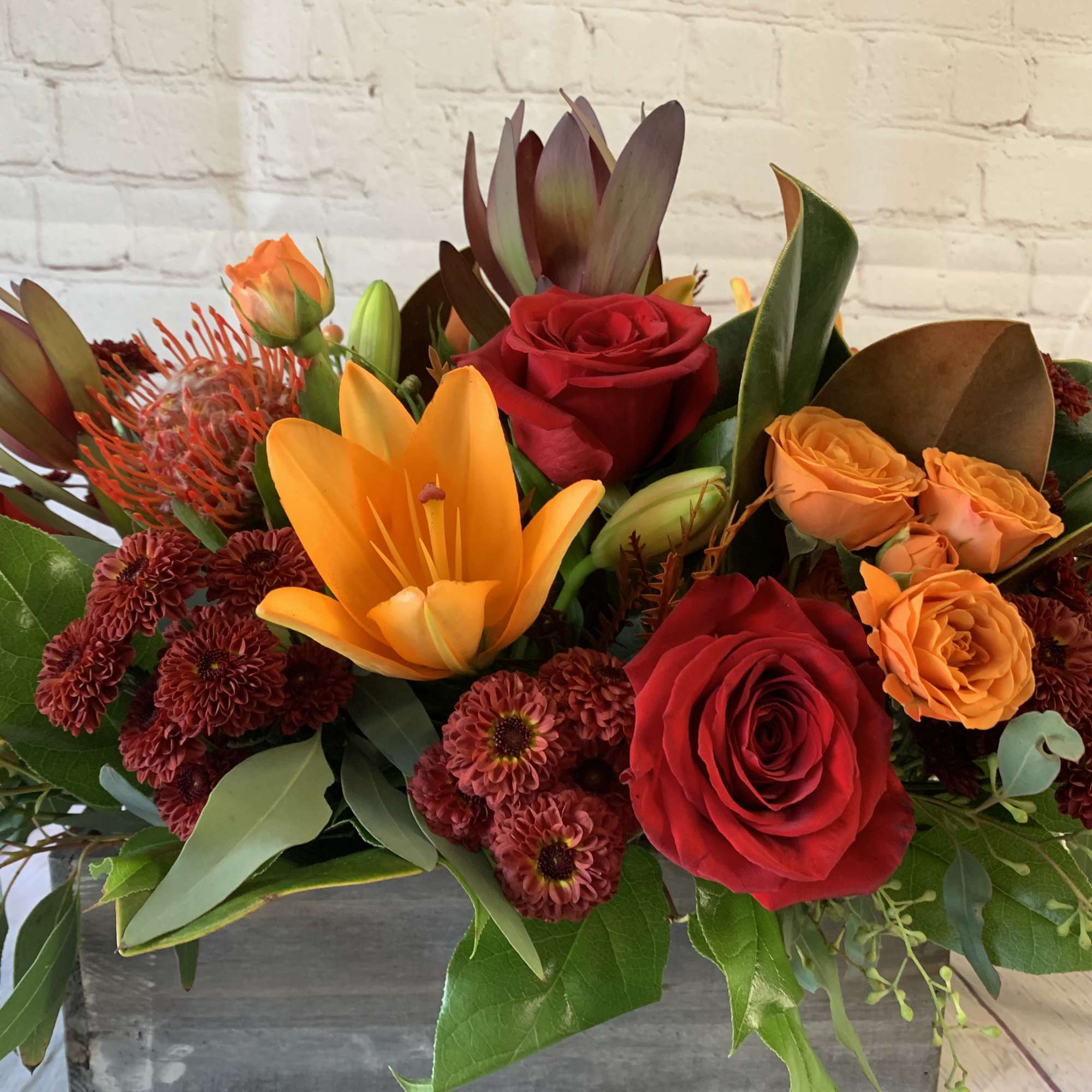 Mixed bouquet with red roses, orange lilies, and burgundy flowers in a rectangular container