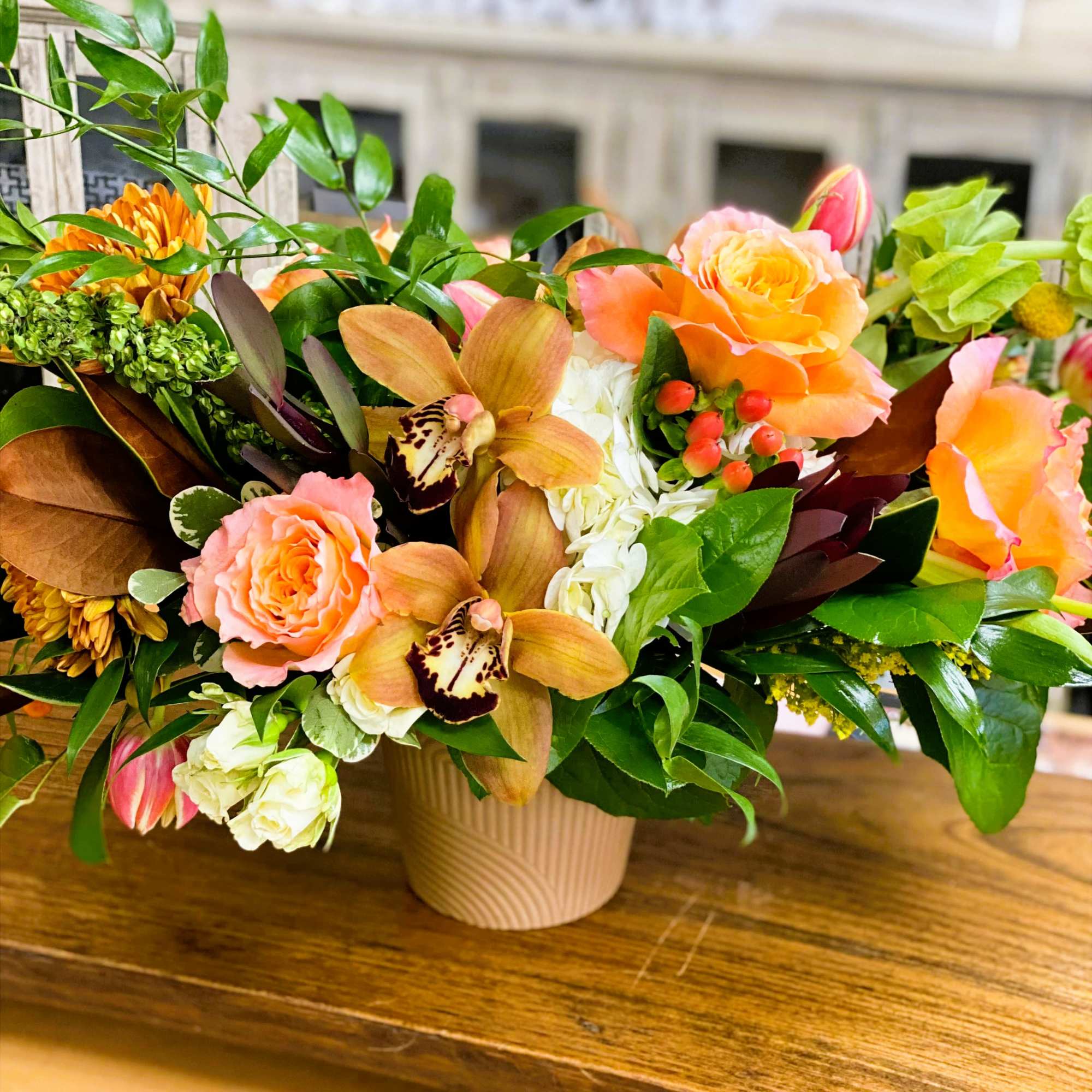 Mixed floral arrangement in a beige vase with peach roses and orchids