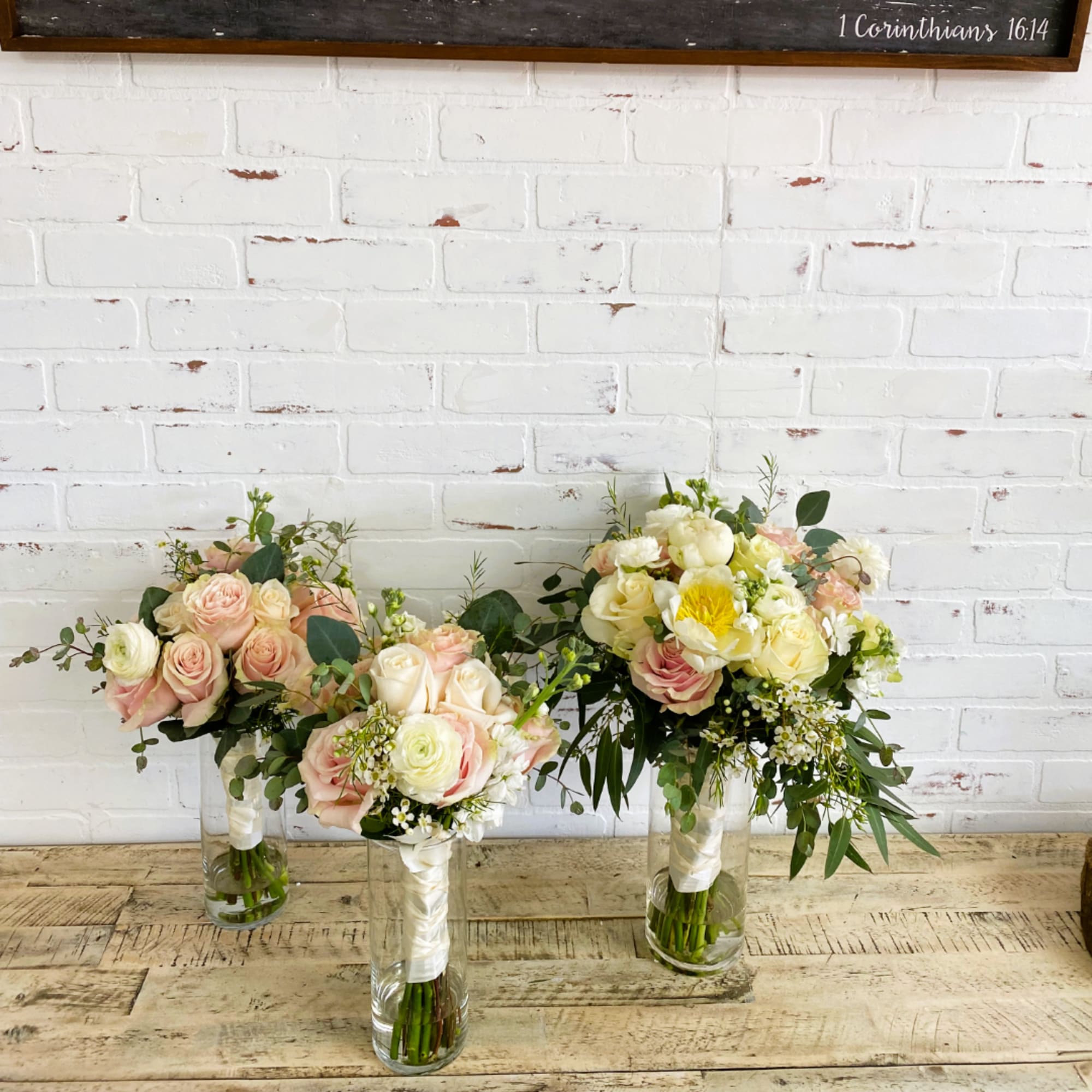 Three pastel rose bouquets in clear glass vases on a wooden table